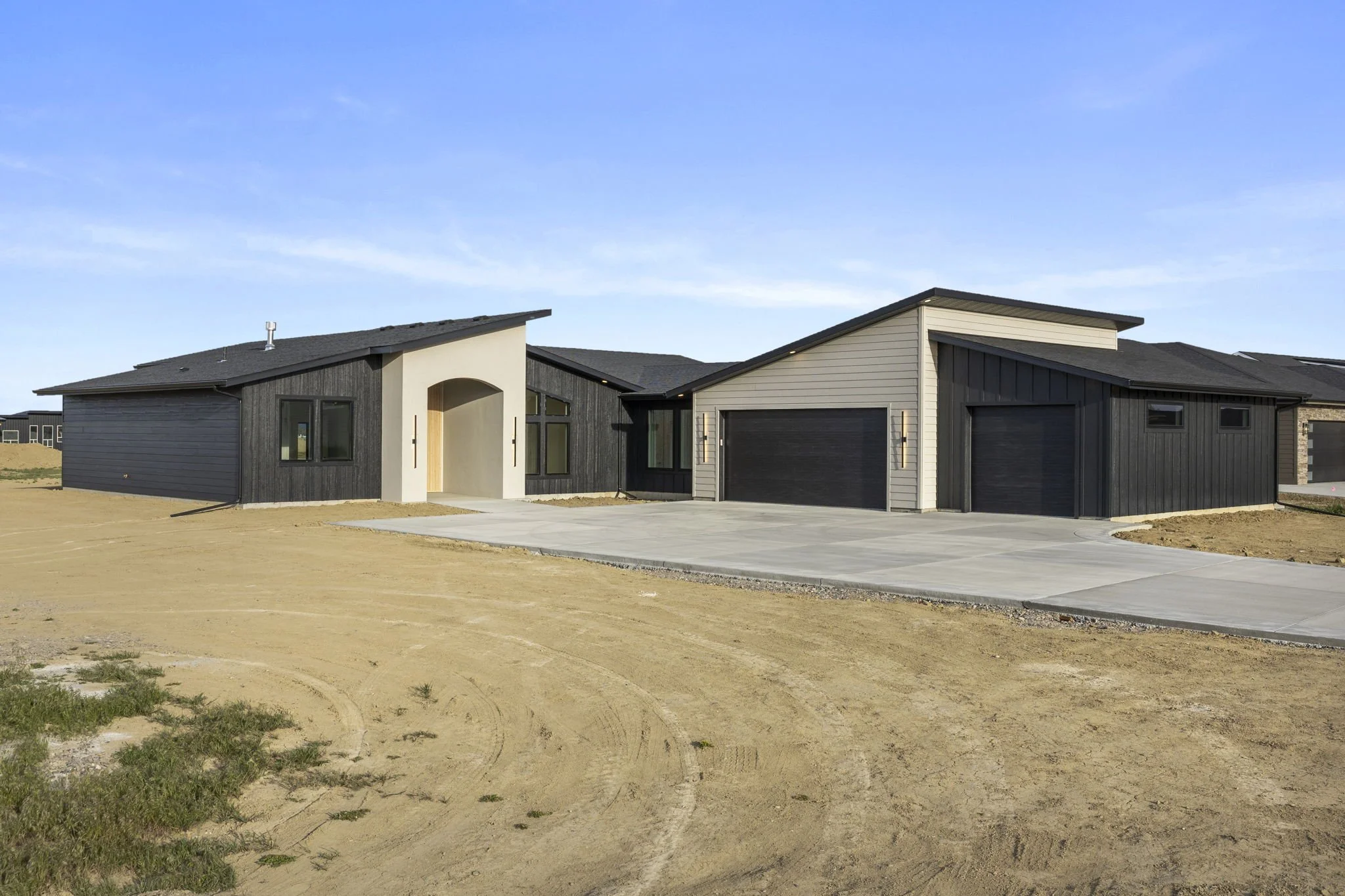 Modern house with dark and light siding, front driveway, and clear blue sky.