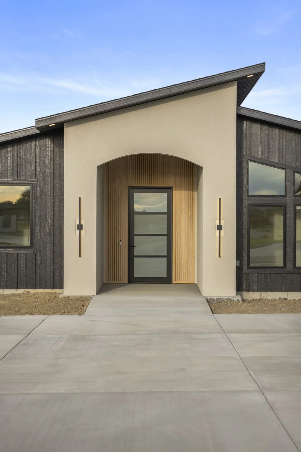 Modern house with a black door, wooden accents, and large windows, under a clear blue sky.