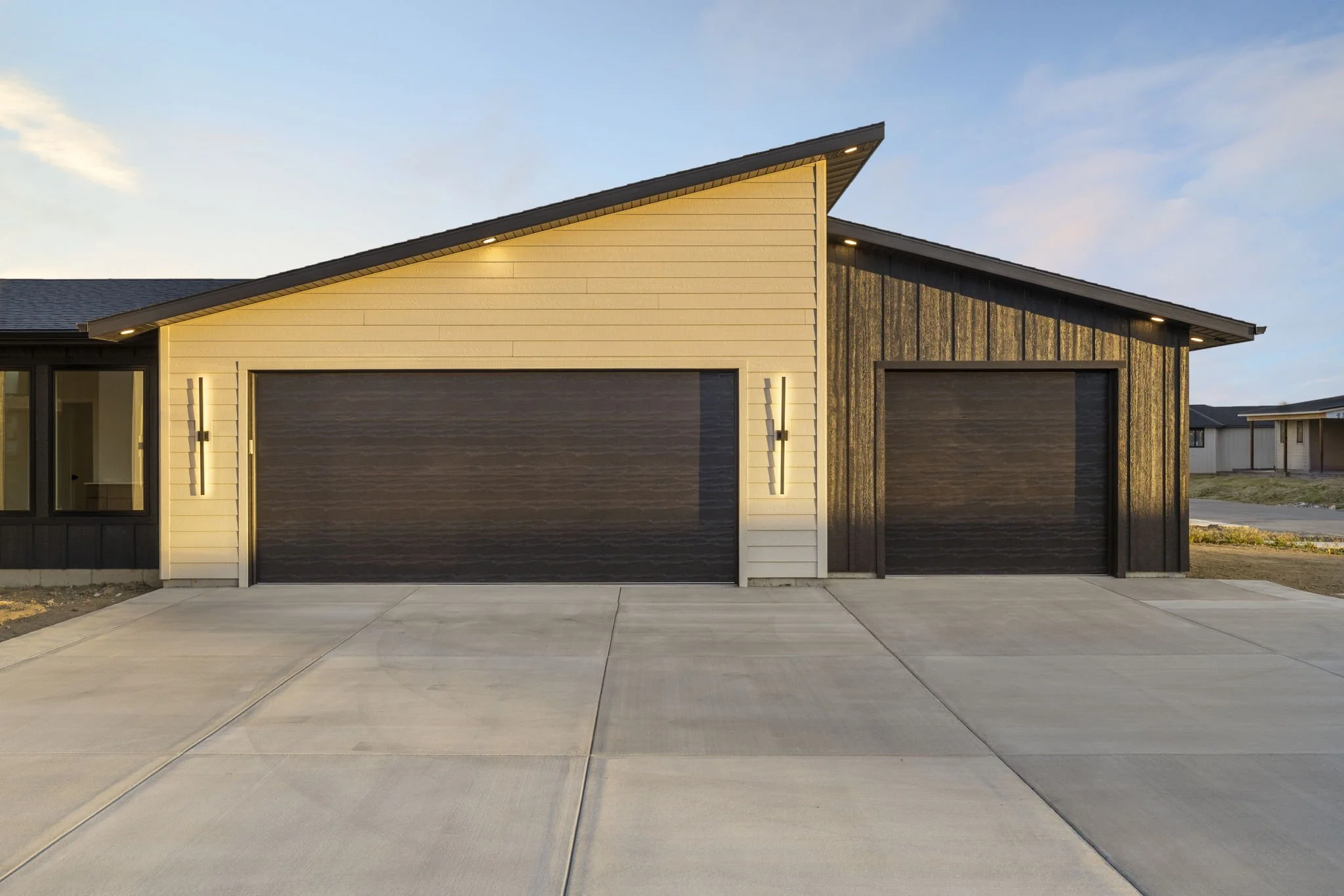 Modern house with two garage doors, exterior lighting, and a concrete driveway, during sunset.