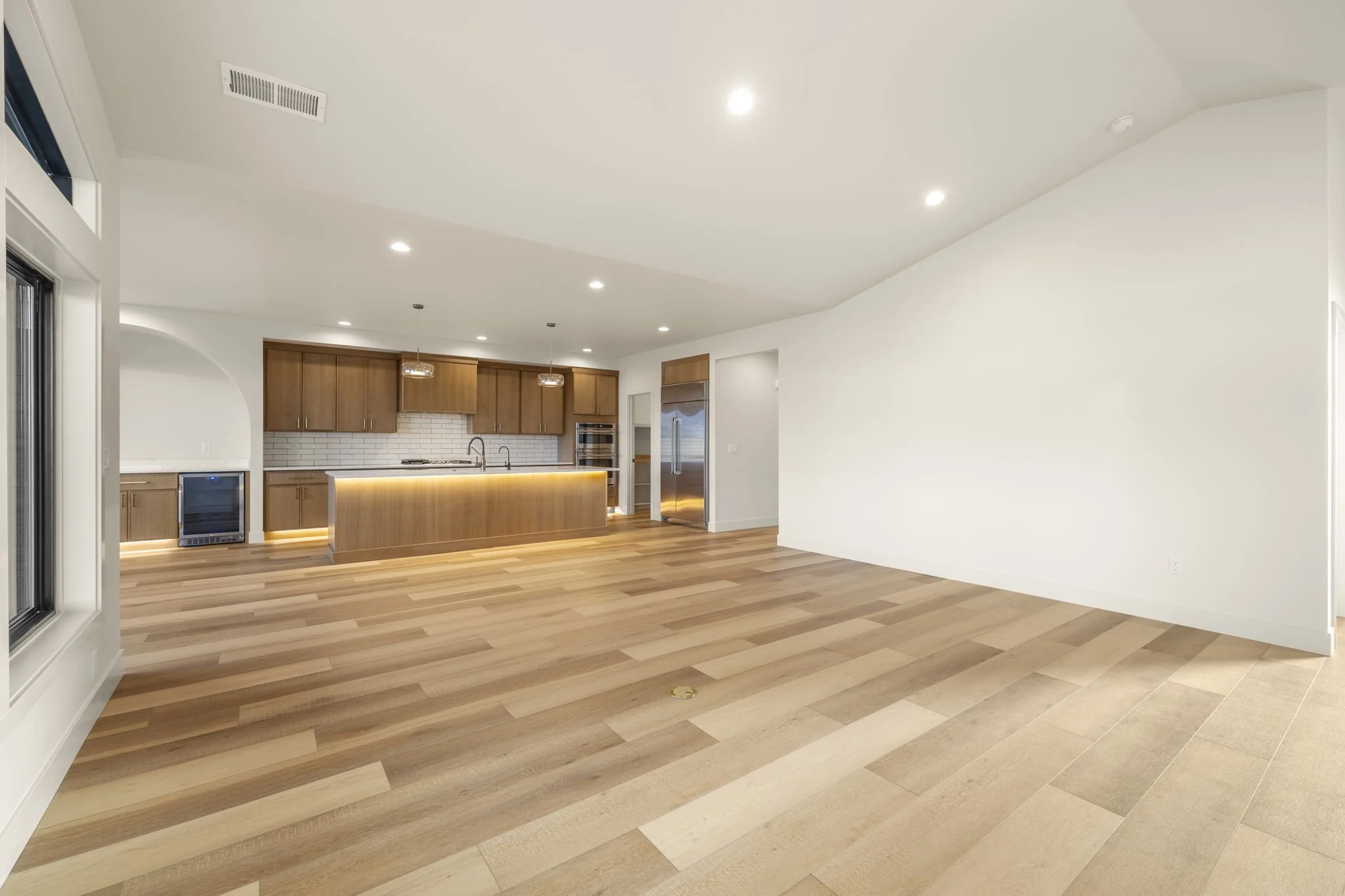 Open kitchen with wooden cabinets, a white subway tile backsplash, an island with lighting underneath, stainless steel appliances, and hardwood floors.