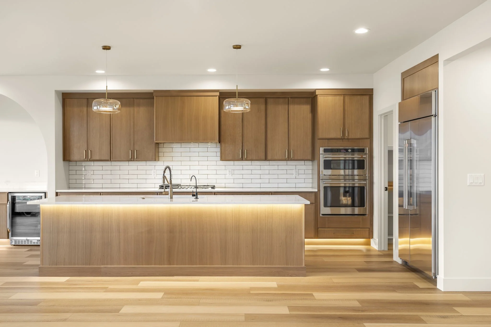 Modern kitchen with wooden cabinets, white subway tile backsplash, a kitchen island with built-in lighting, stainless steel appliances, and hardwood floors.