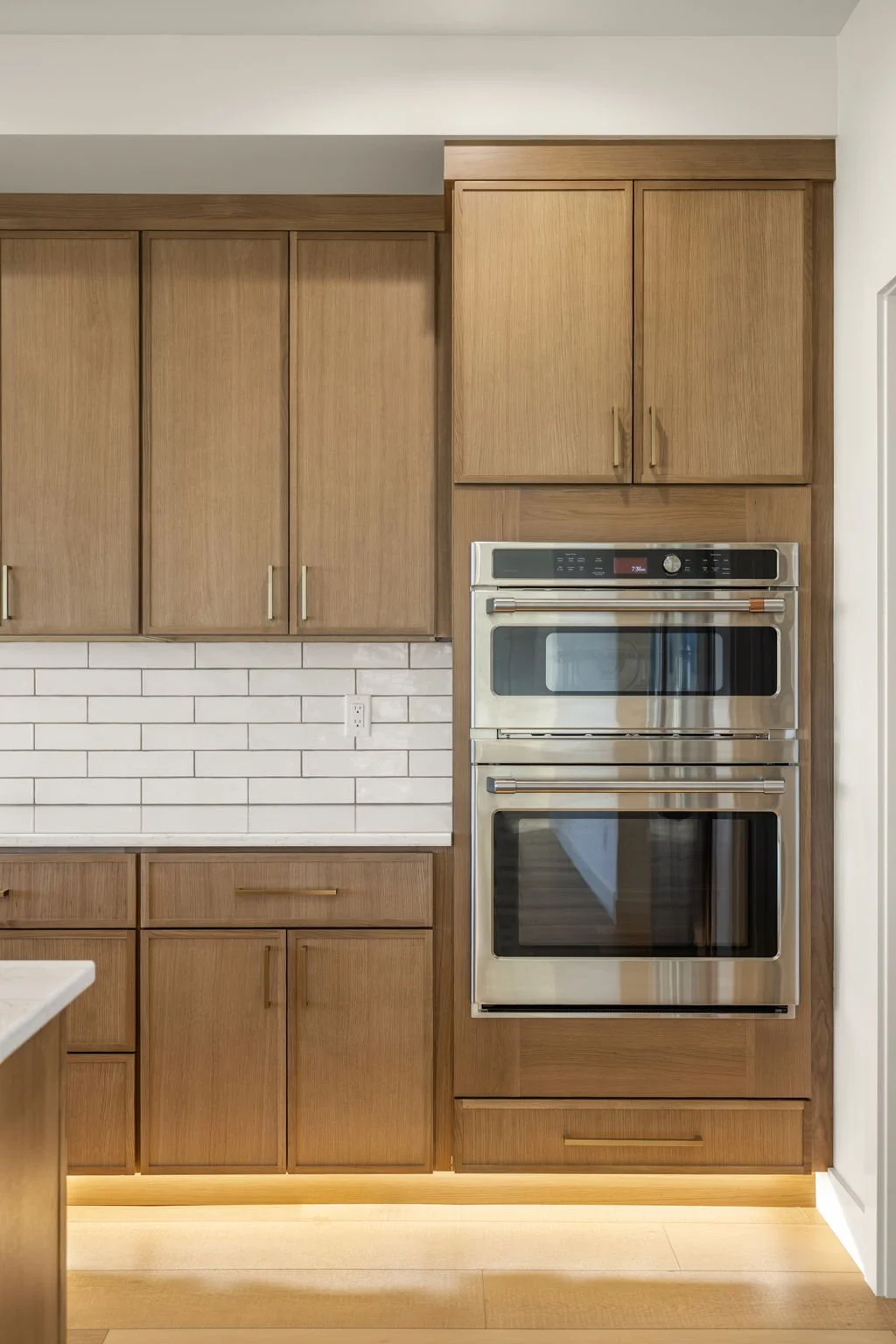Kitchen with wooden cabinets, white tiled backsplash, and built-in stainless steel double oven.