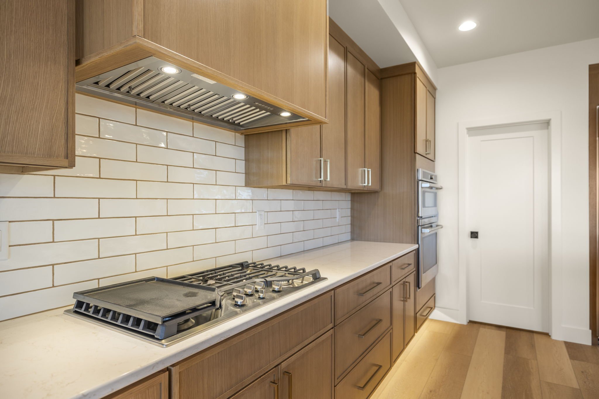 Modern kitchen with wooden cabinets, white subway tile backsplash, gas stove, and built-in oven.