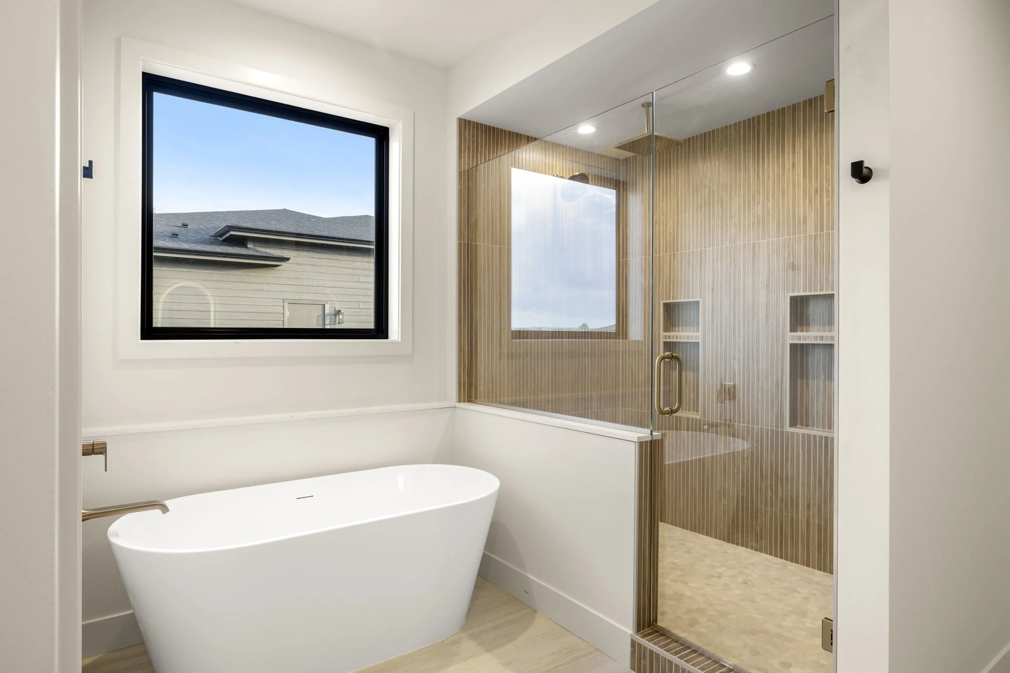 Modern bathroom with a white freestanding bathtub, a large window, and a walk-in shower with glass and wood paneled walls.