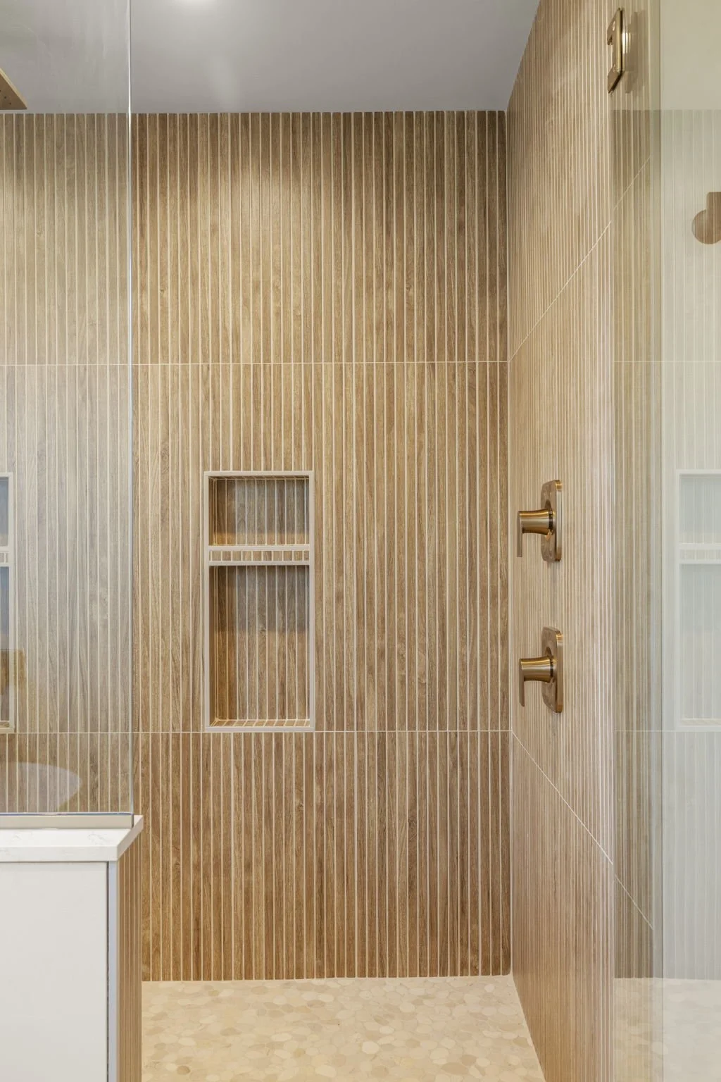 Modern walk-in shower with vertical wood-look tiles, a built-in shelf, and gold shower fixtures.