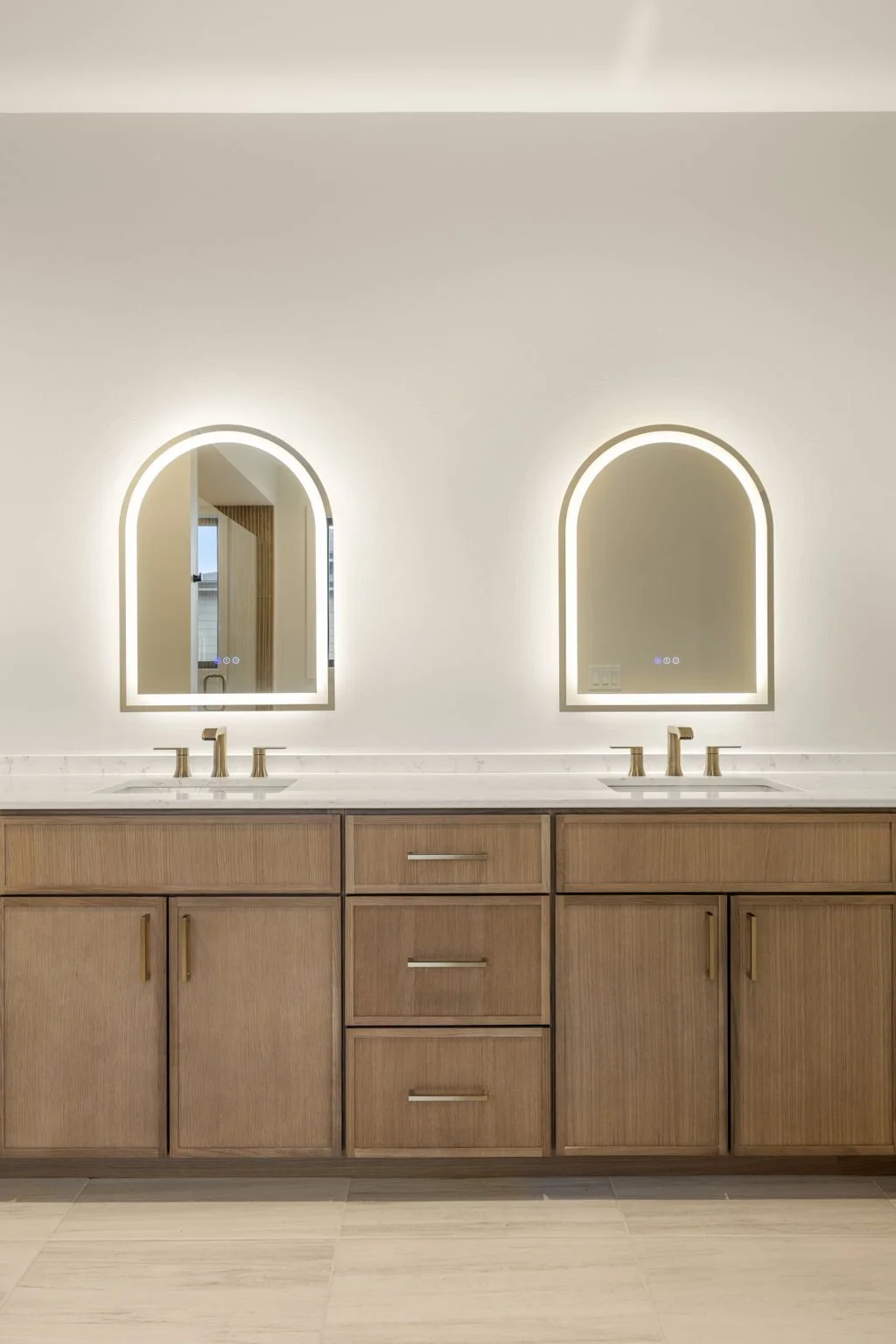Double bathroom vanity with lighted mirrors, wooden cabinets, and two sinks.