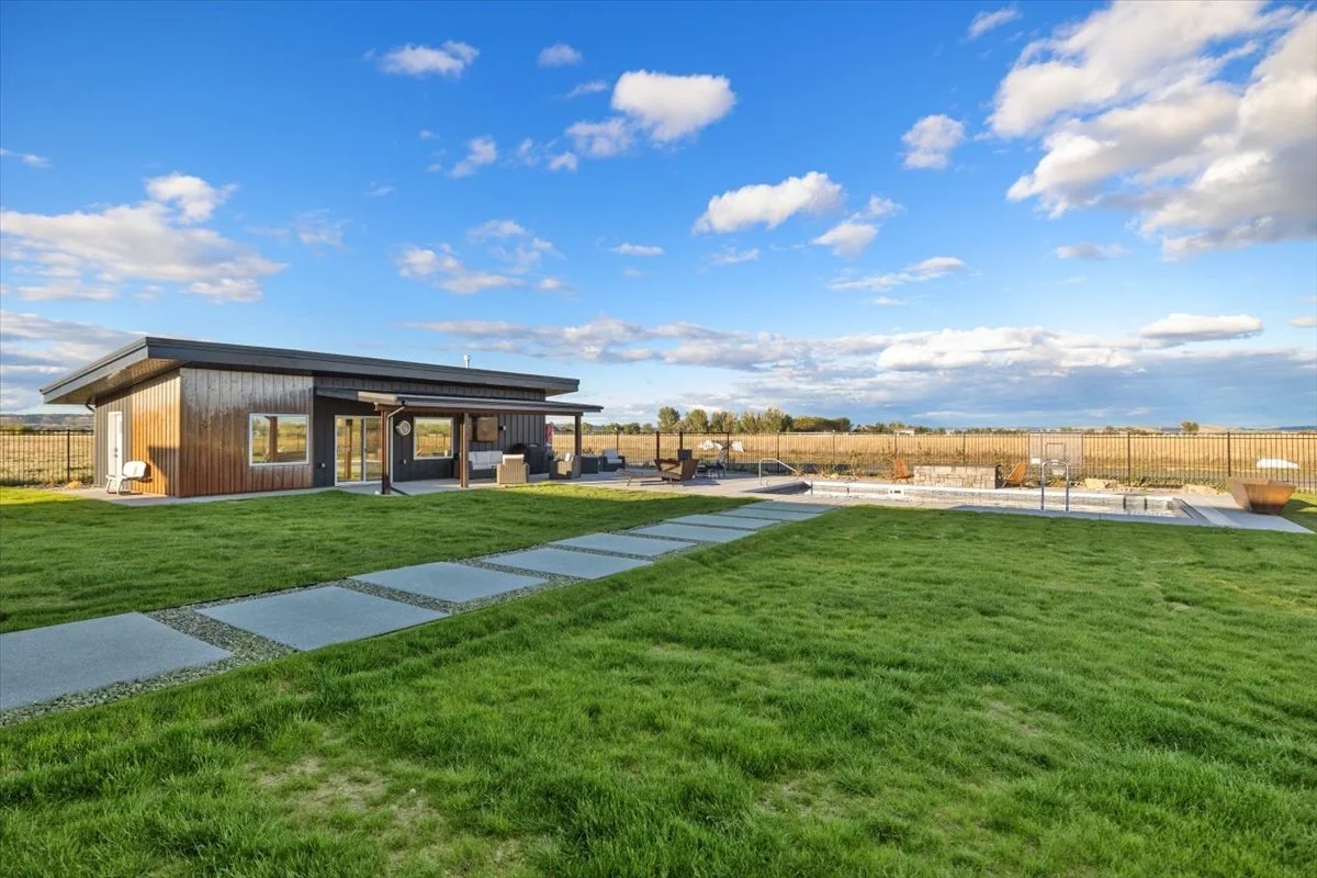Modern backyard with a house, a paved walkway, a swimming pool under construction, outdoor furniture, and a fence in the background under a partly cloudy sky.
