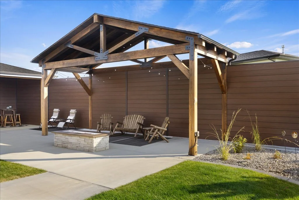 Open kitchen and living area with light wood cabinets, a large island with four chairs, pendant lighting, a sofa, and a dining table near a large window.