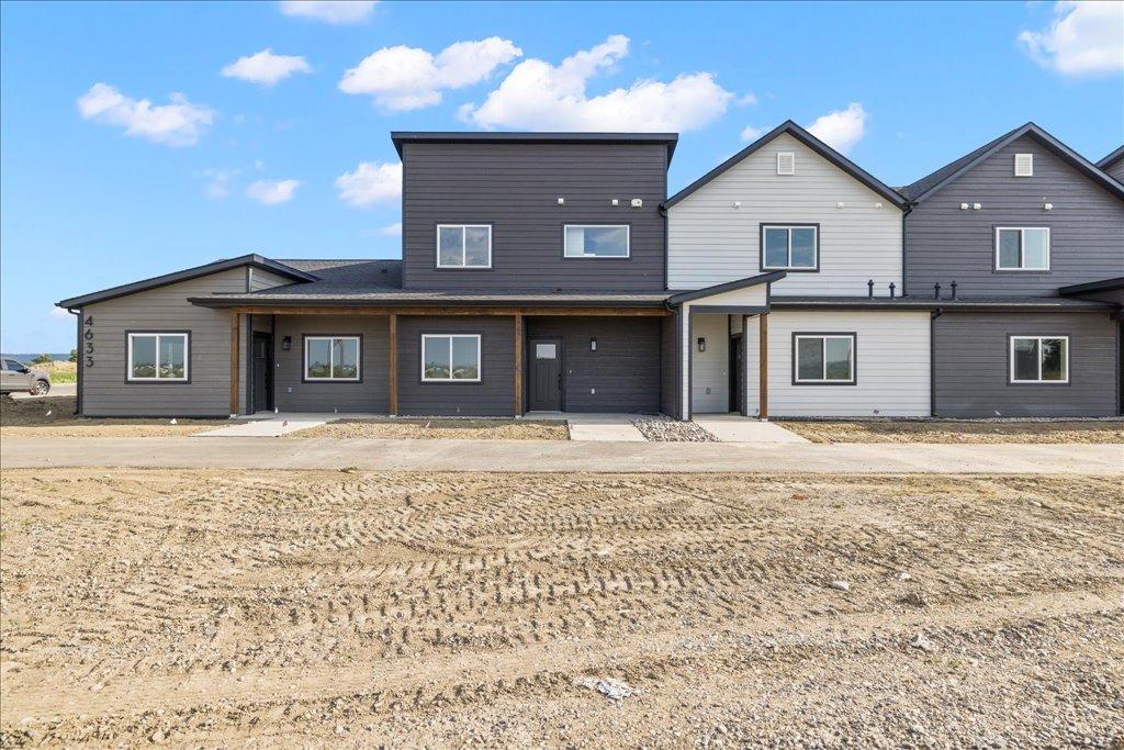 Modern multi-unit townhouse complex with gray and white siding under a partly cloudy sky, featuring multiple windows and doors.
