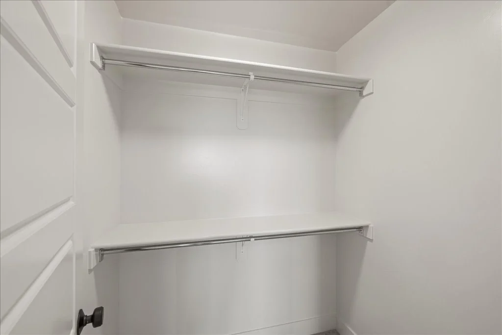 Empty white closet with two shelves and hanging rods.