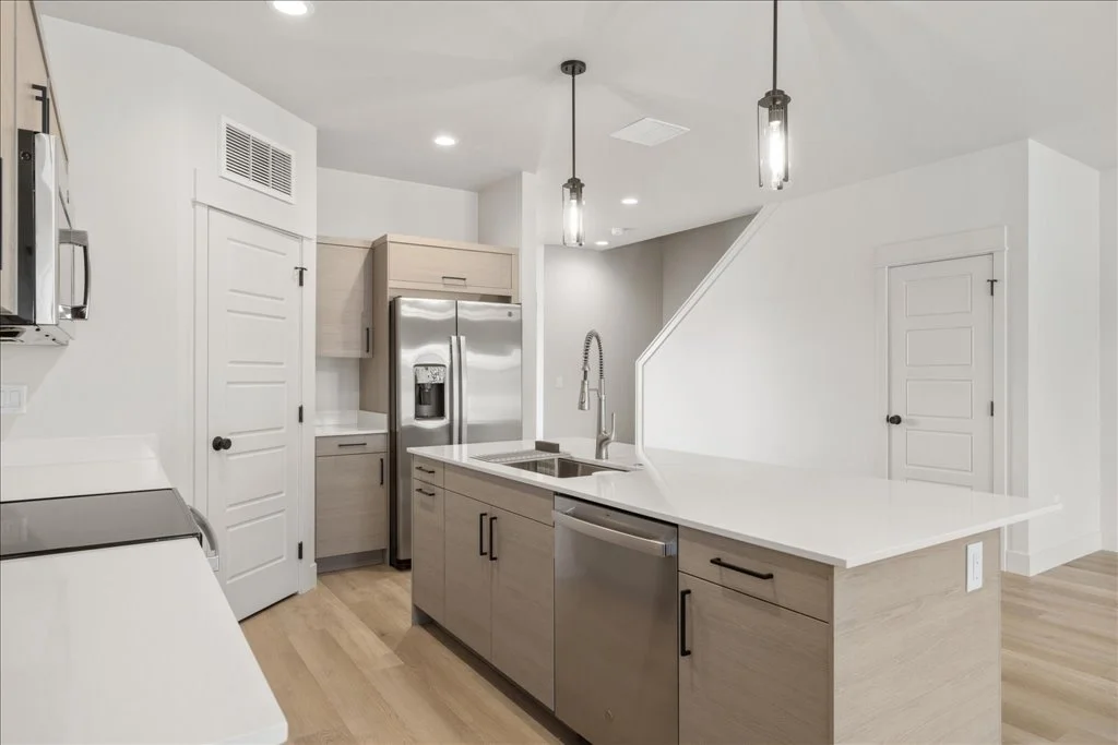 Modern kitchen with white counter, light wood cabinets, stainless steel appliances, and pendant lights.