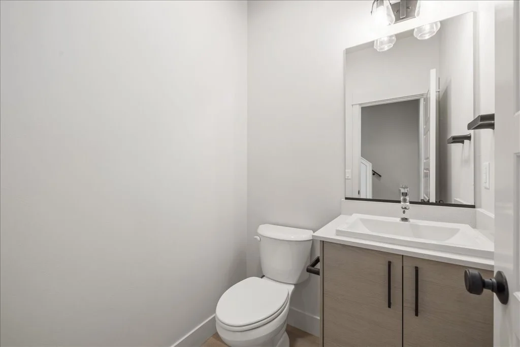 Modern bathroom with a white toilet, a vanity with a sink and a mirror, and a wall-mounted light fixture.