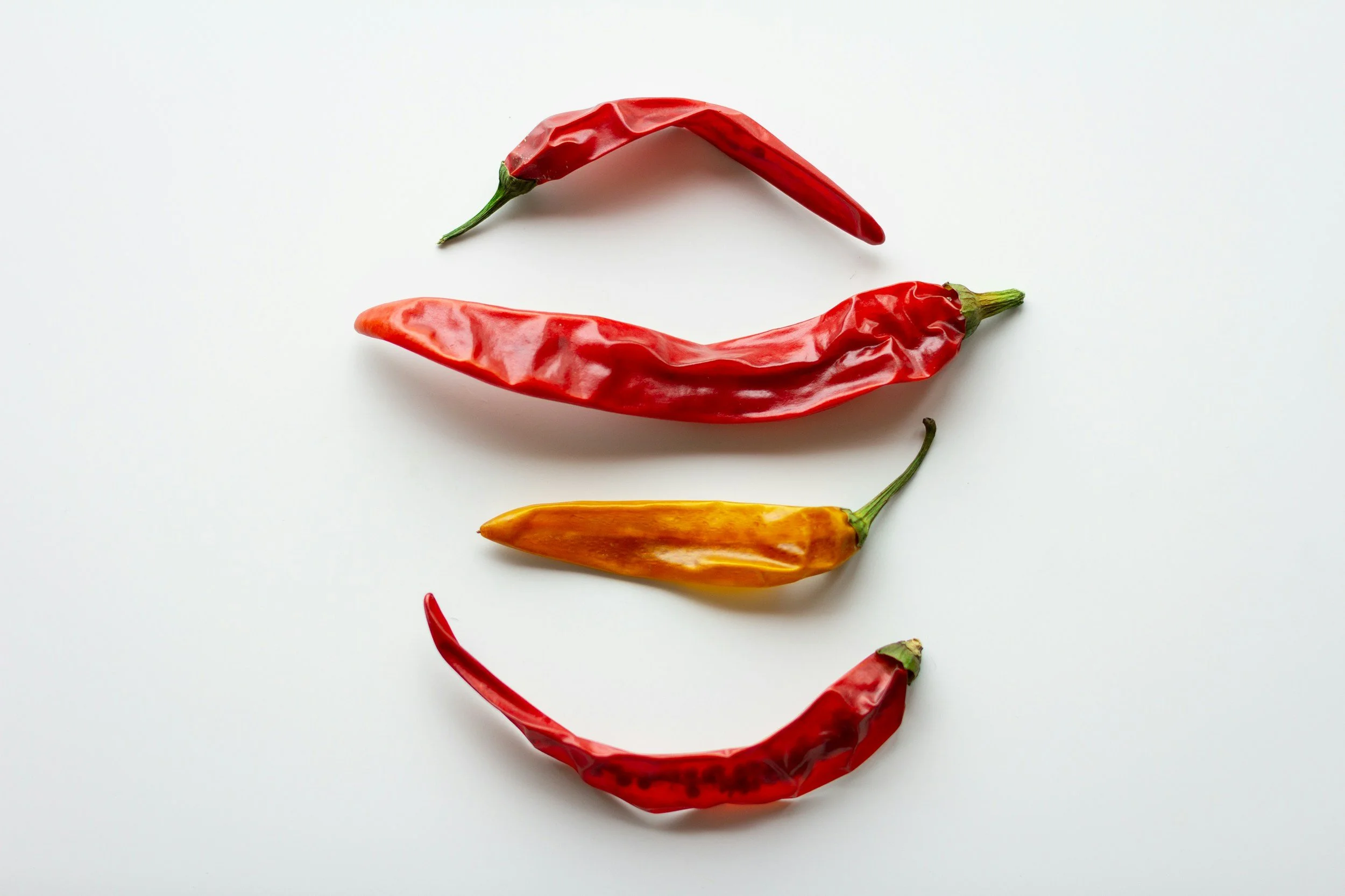 Five chili peppers arranged to resemble a smiley face, with three red peppers and one orange pepper set against a white background.