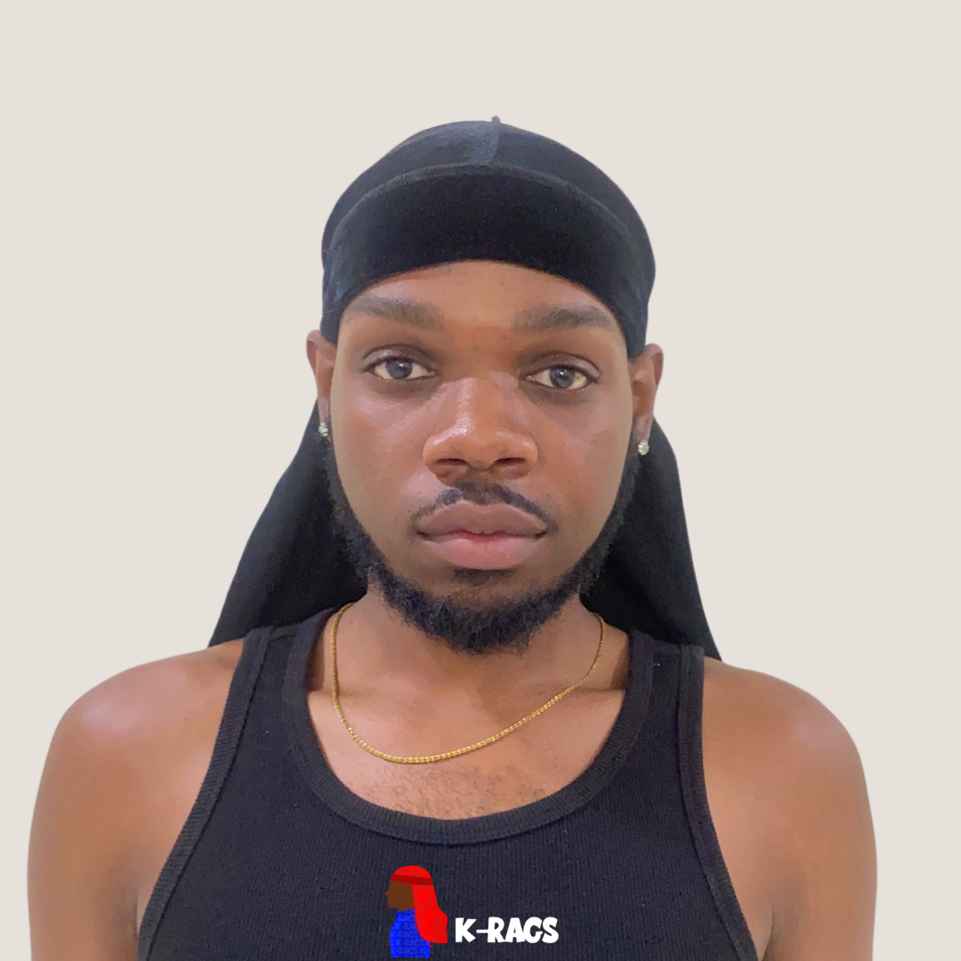Portrait of a young man wearing a black durag, black tank top with a logo, a gold chain, and diamond earrings, against a plain white background.