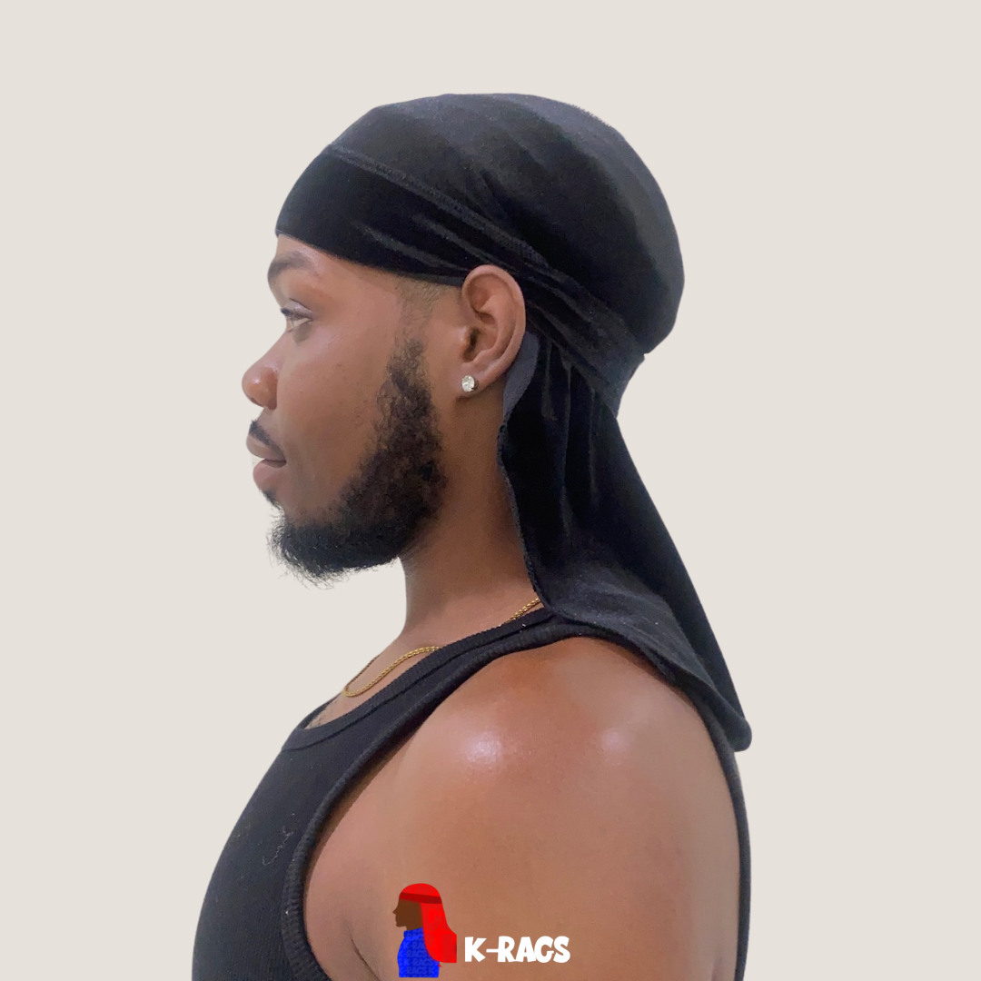 Side profile of a man with a beard and earrings wearing a black durag and black sleeveless shirt against a plain background.