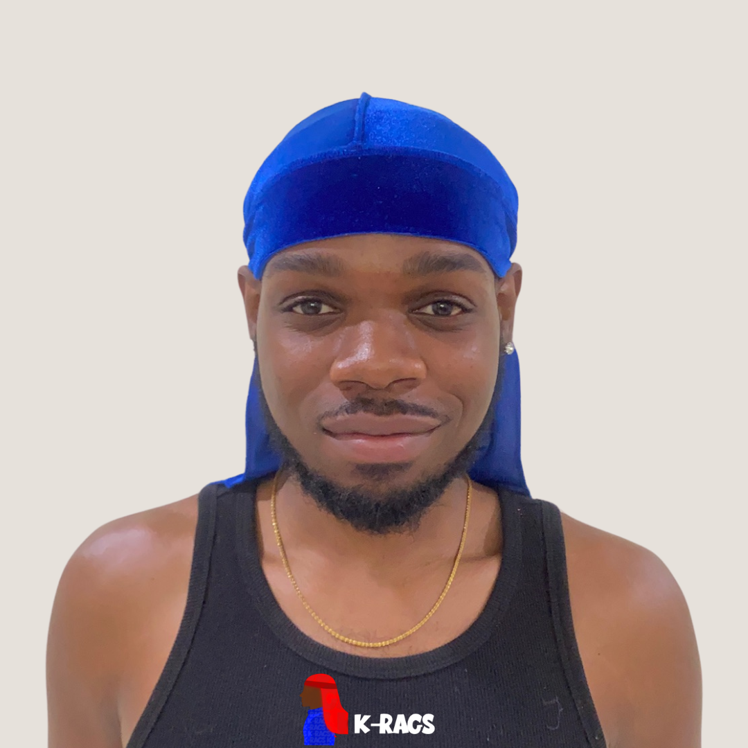 A young man wearing a blue durag, black tank top, and a gold chain, smiling at the camera with a plain light-colored background.