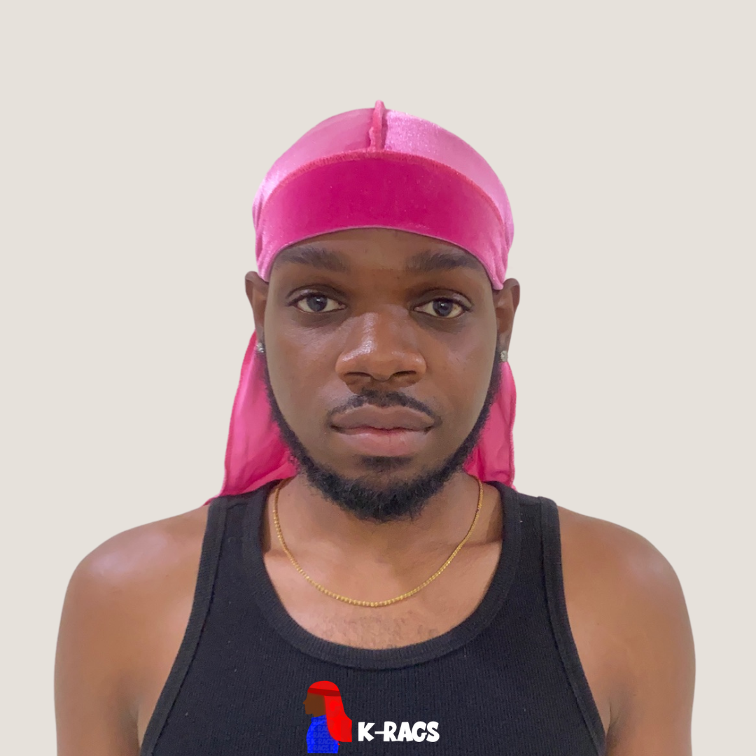 A young man wearing a pink durag and a black tank top, looking directly at the camera with a neutral expression. Background is plain off-white.