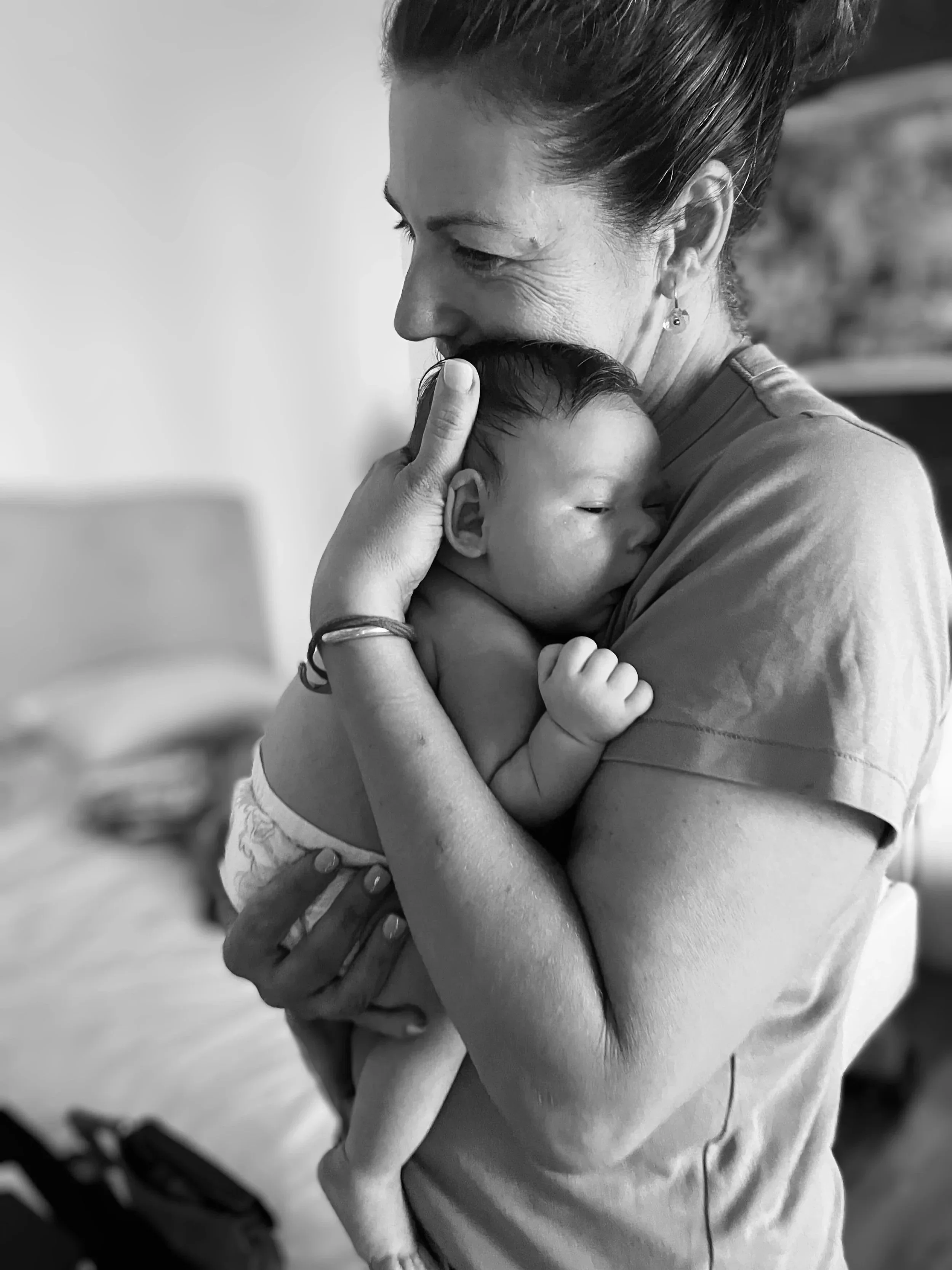 A woman holding a sleeping baby close to her chest, gently touching the baby's head with her finger.