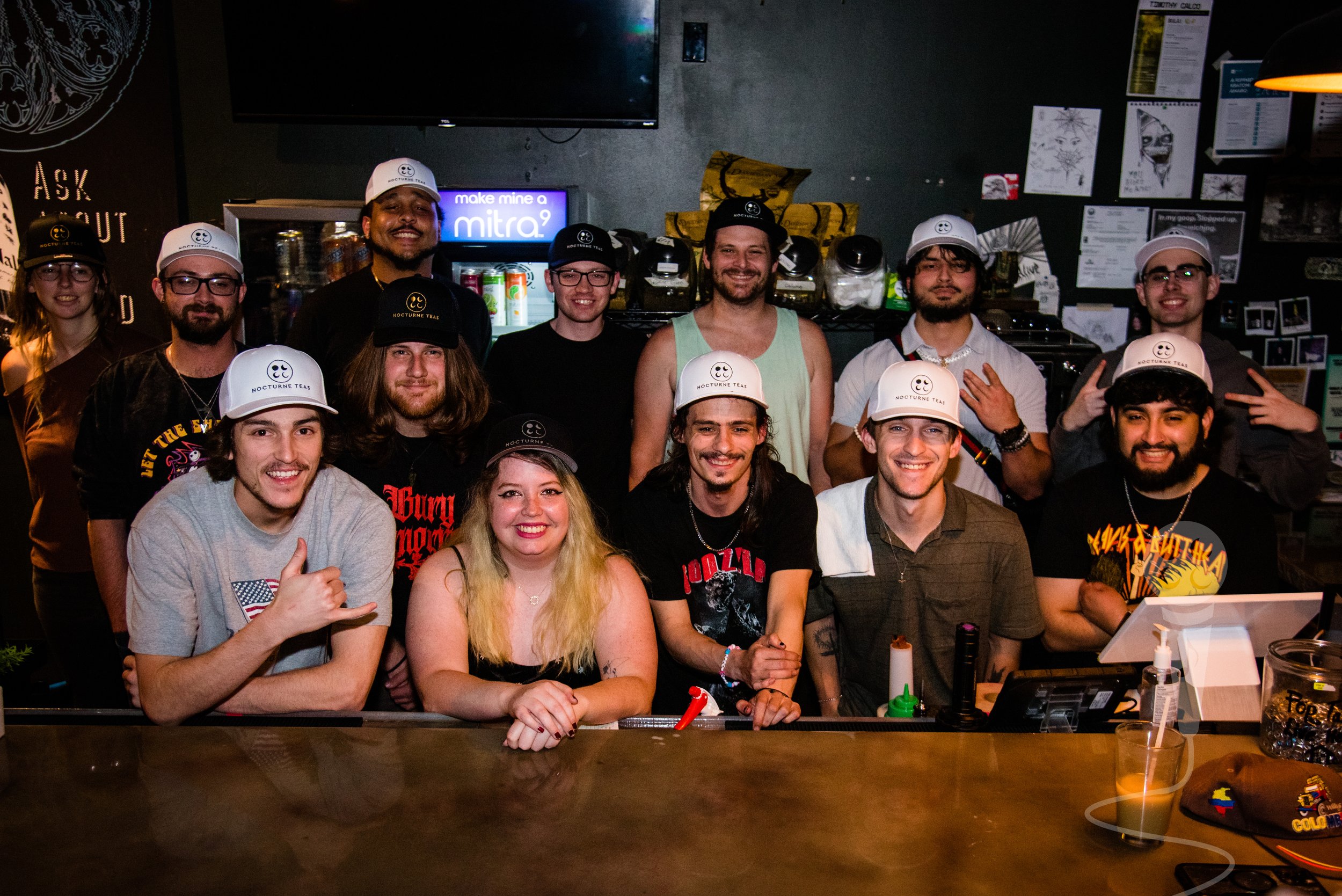 A group photo of 13 people, all wearing white hats with the embroidered text "Nocturne Teas"