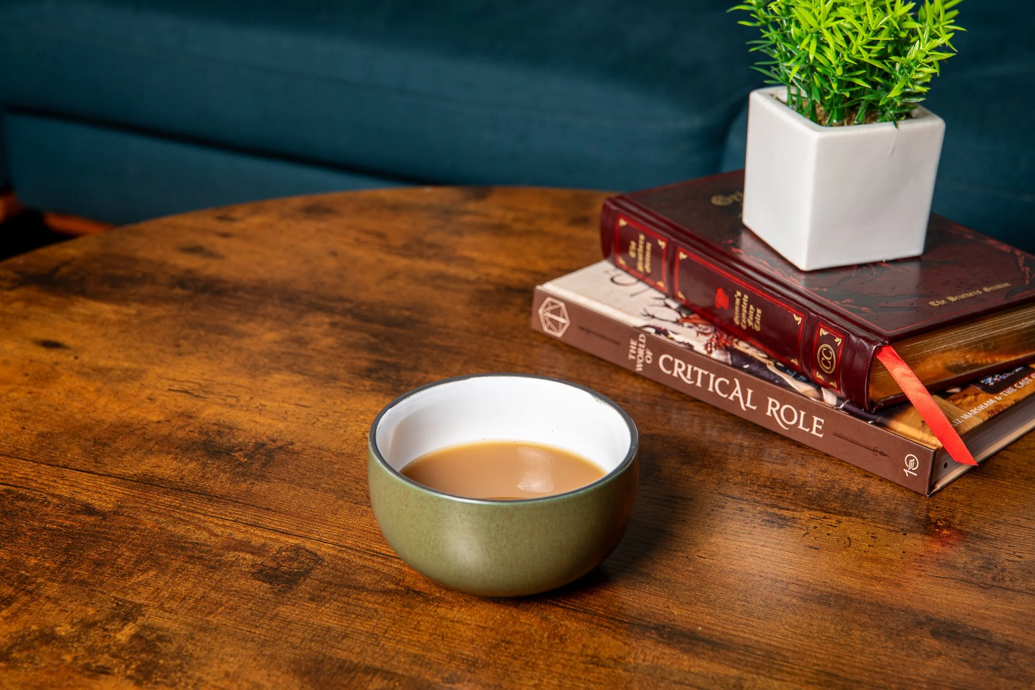 A bowl of kava sitting on a wood table with two books in the background. It is a stoneware bowl and is filled halfway with kava.