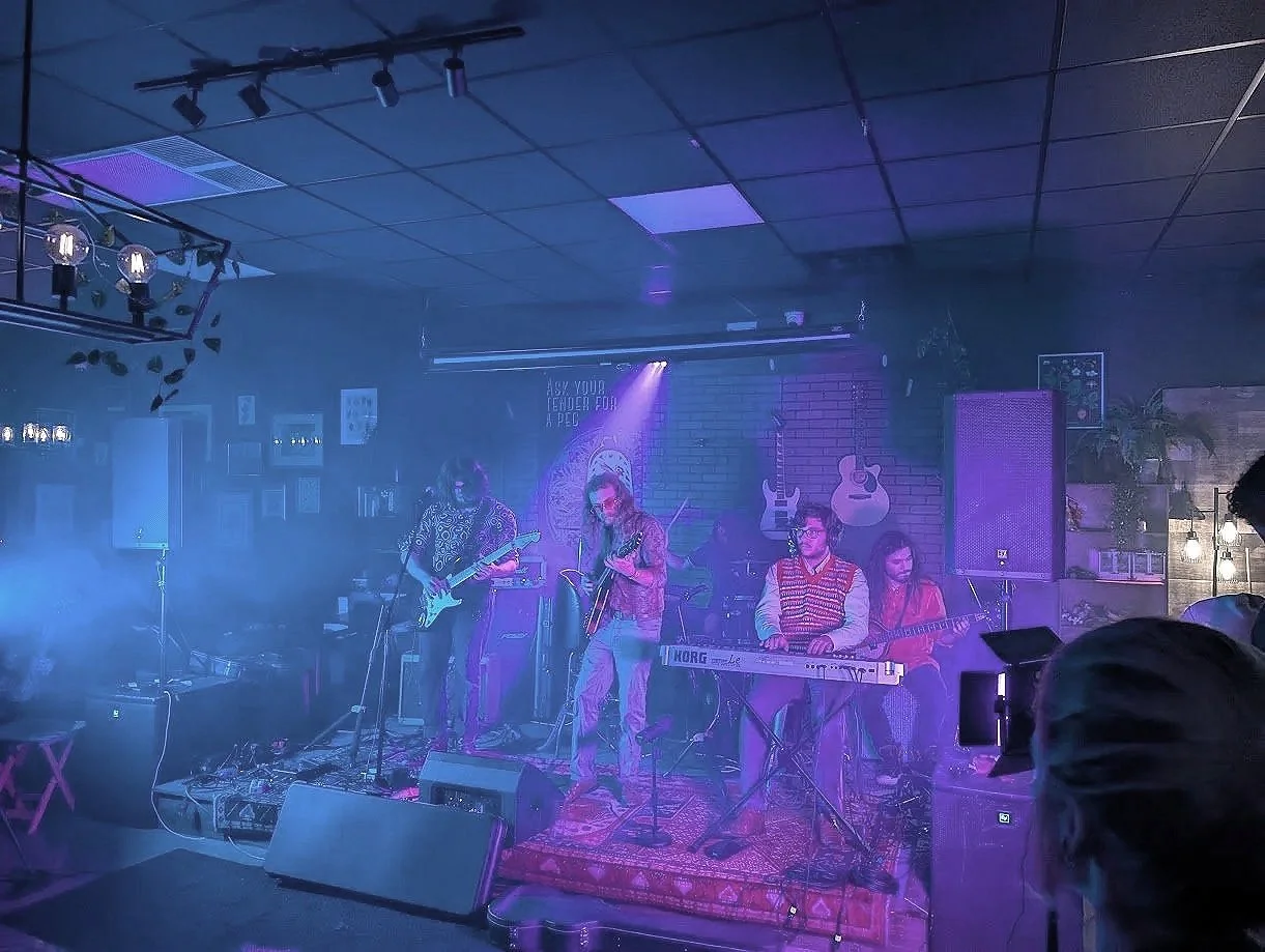 A band performing on a stage with color flights and fog effects.