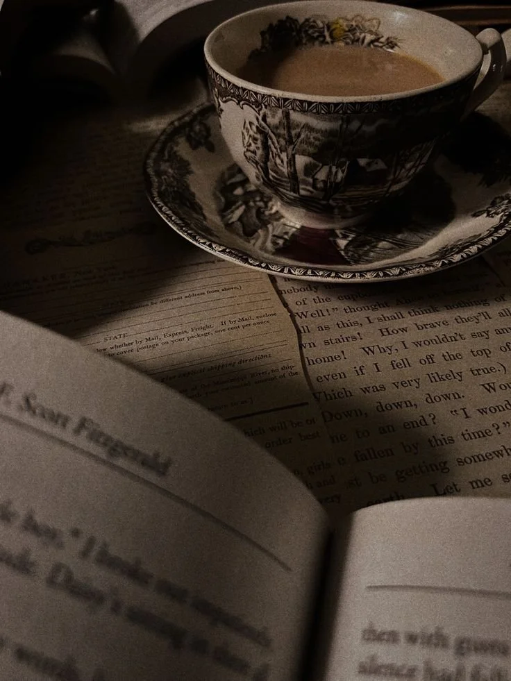 A cup of tea on a saucer resting on an open book, with sunlight casting shadows on the pages.
