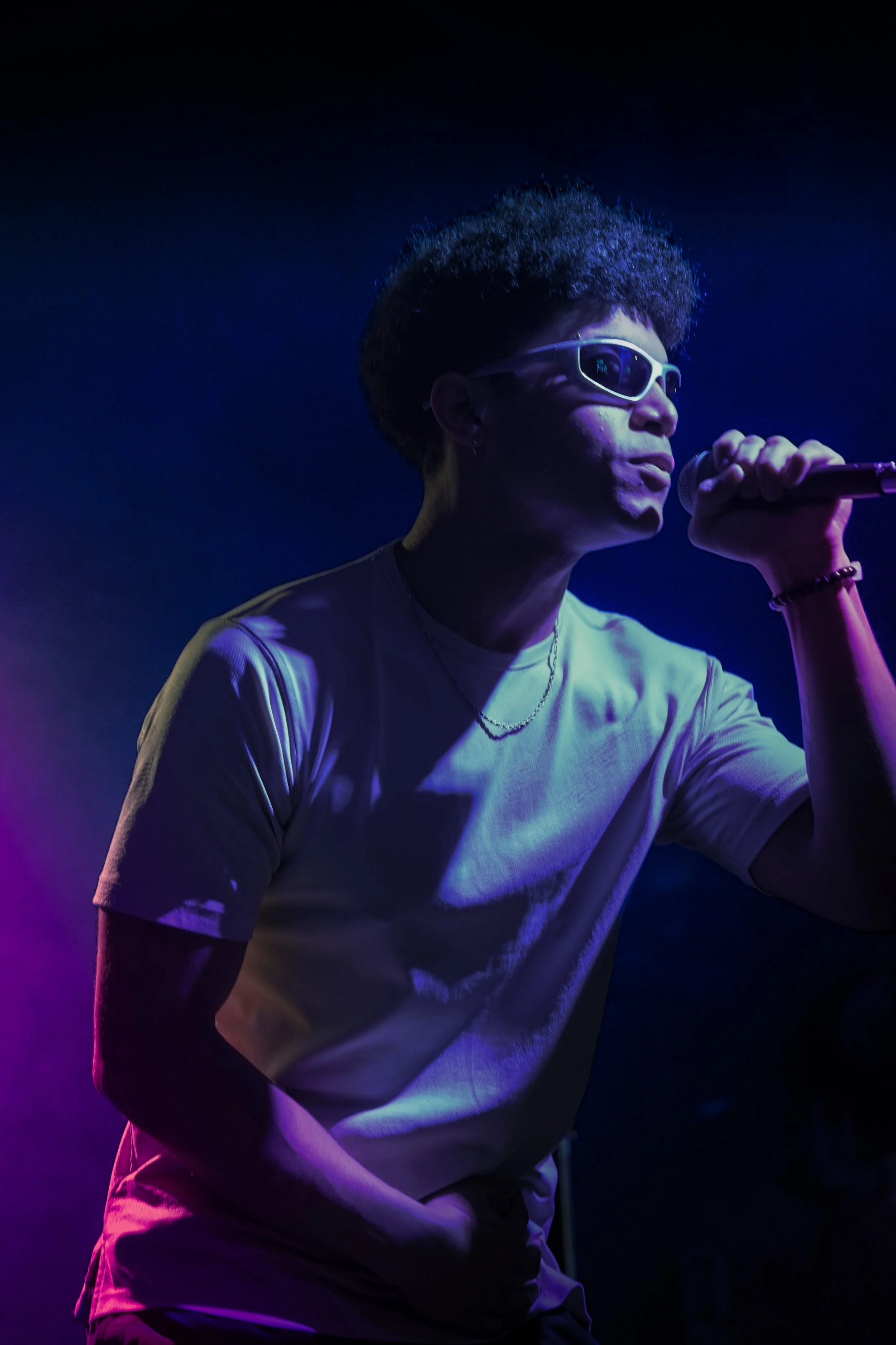 A man wearing sunglasses singing into a microphone