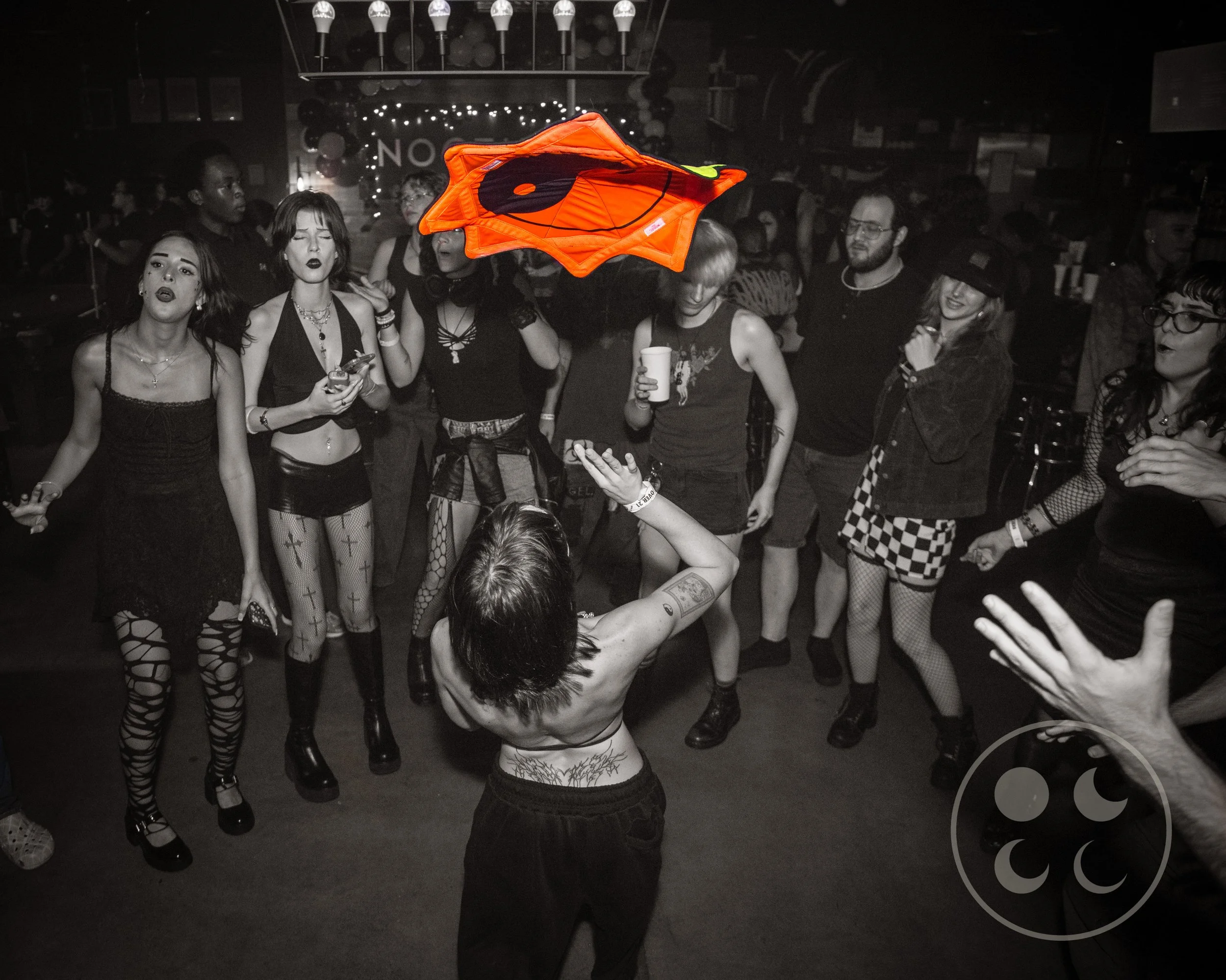 A person performing a trick with a star shaped cloth while an audience formed in a horse shoe watches.