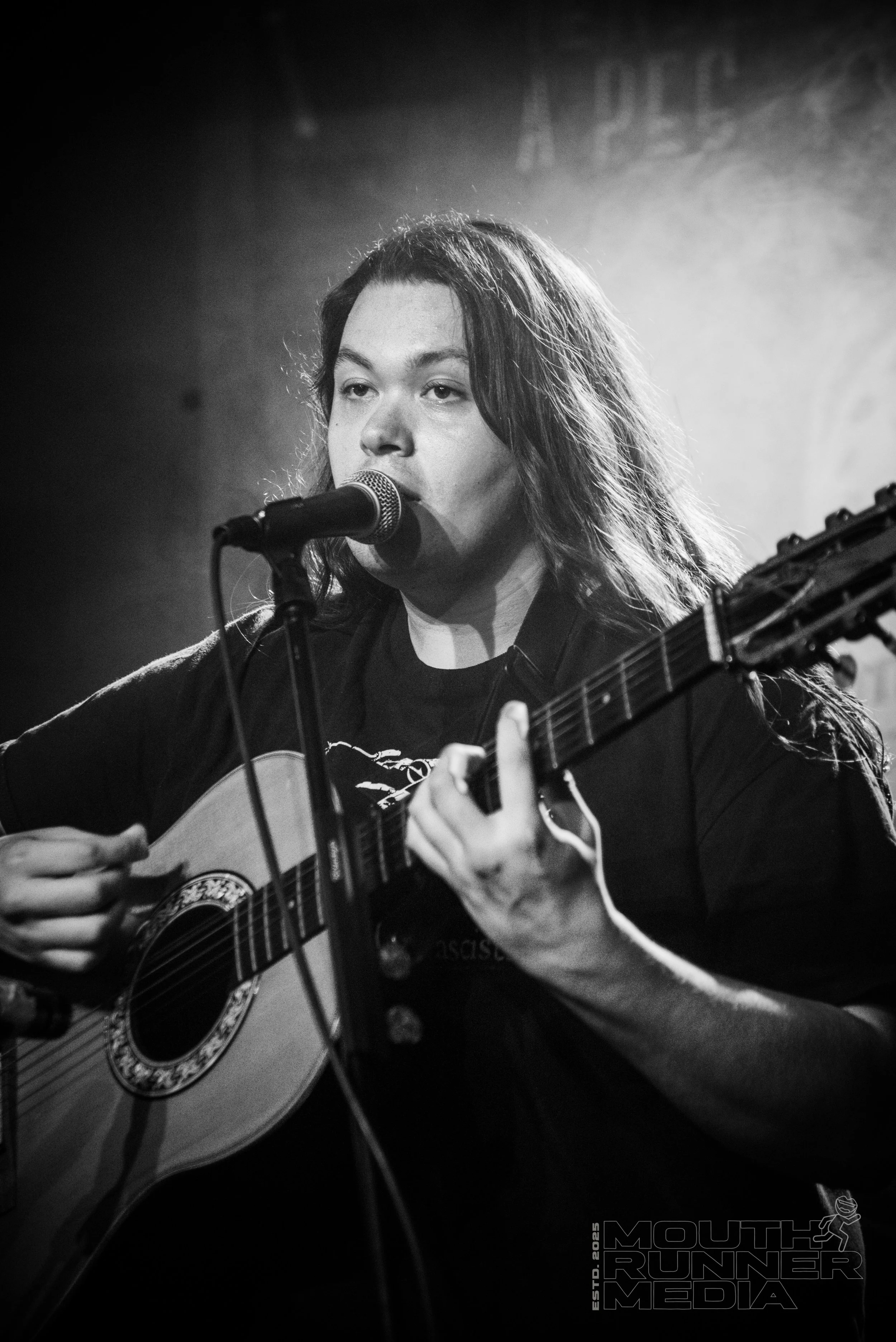 A long haired man singing into a microphone and playing guitar