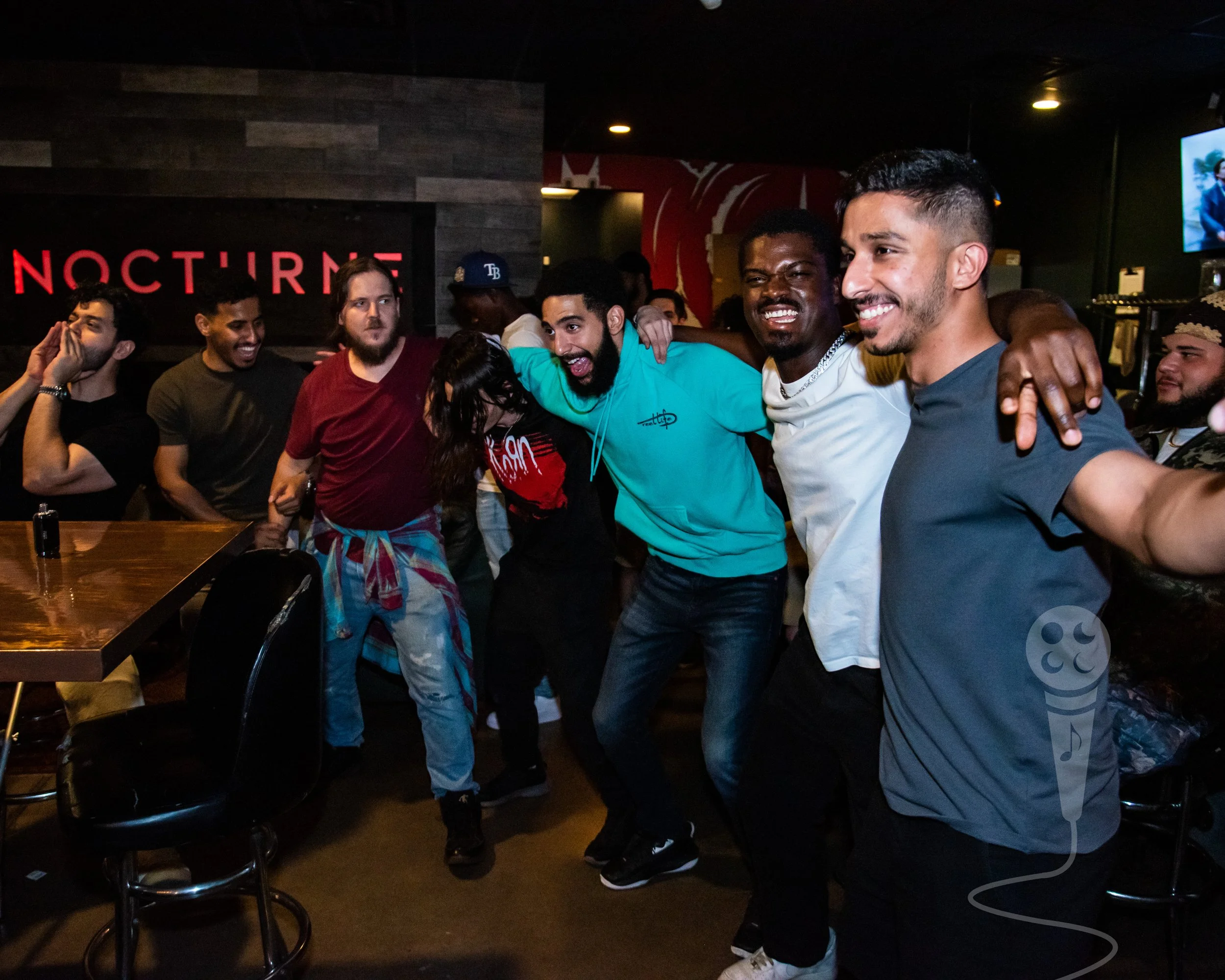 A group of seven people standing with their hands on each others shoulders, all smiling