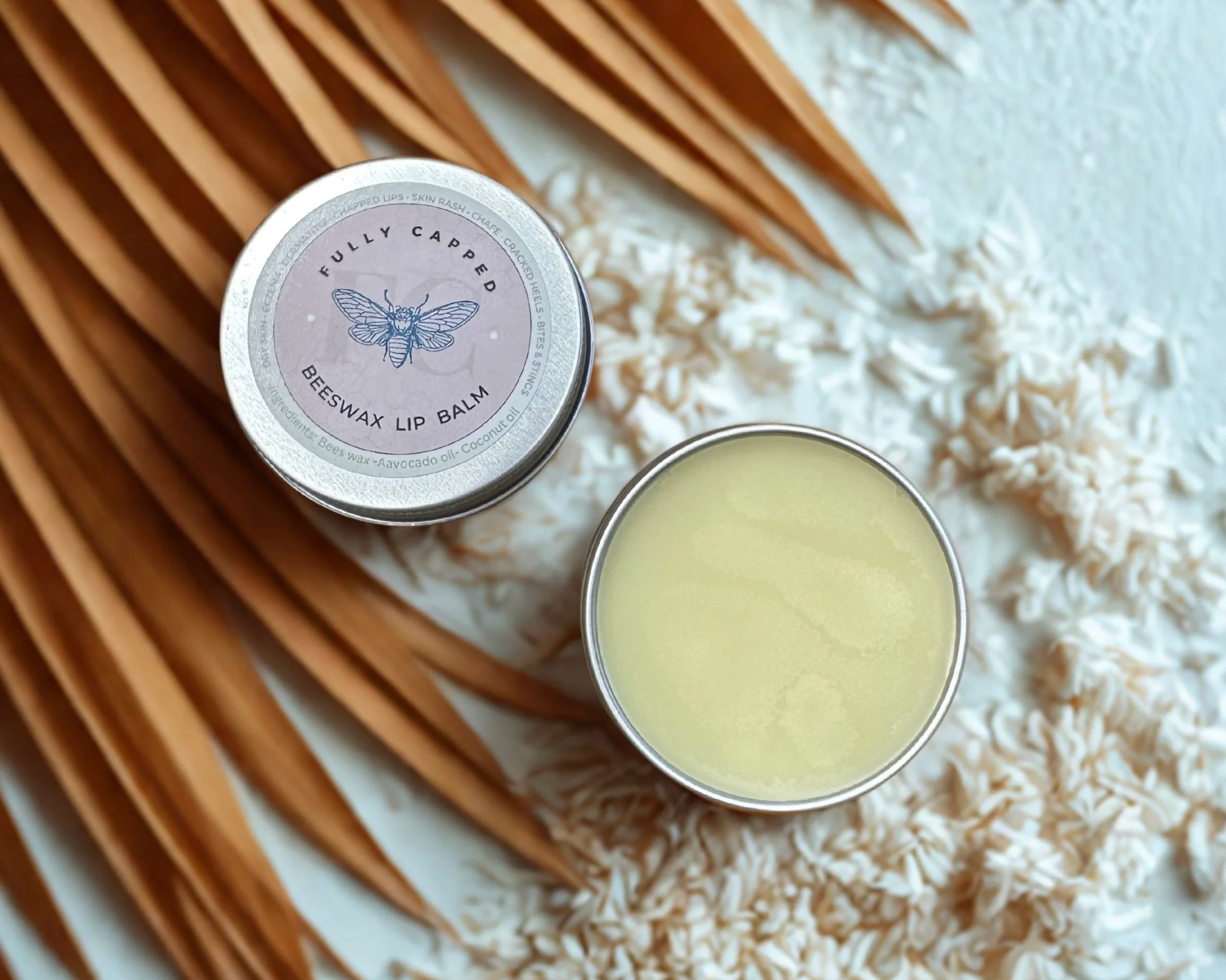 A tin of fully capped beeswax lip balm with a bee illustration, resting on white shredded paper, with wooden slats in the background.