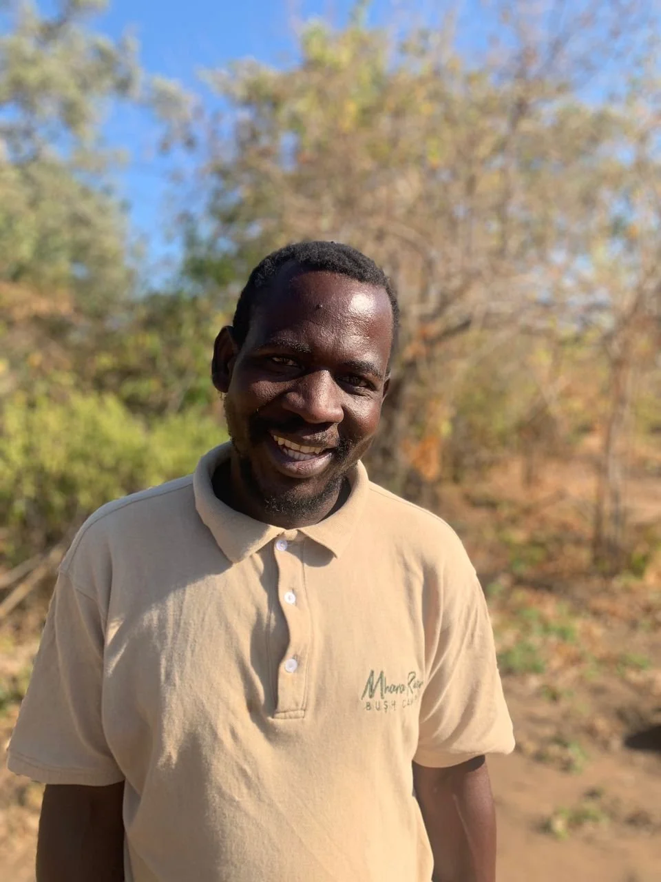 Smiling man outdoors with trees and clear sky in the background