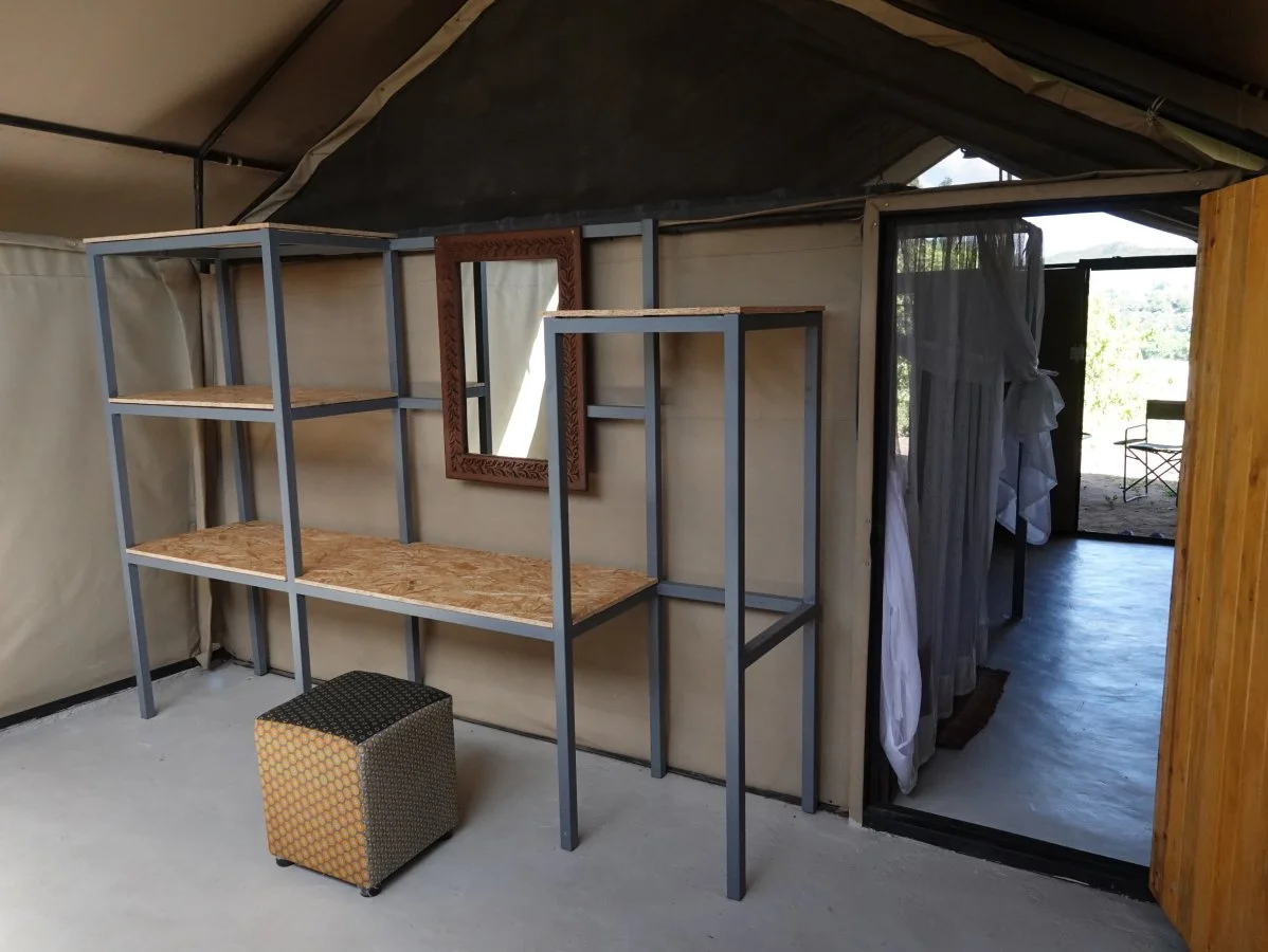 Empty room with metal and wood shelving, a small upholstered cube, and a doorway with curtains leading outside.