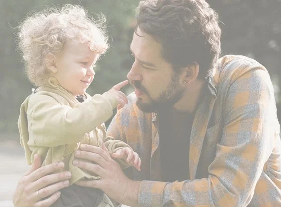 A father and son outside, with the boy touching his dad's nose, sharing a tender moment.