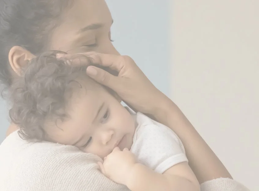 A woman holding a young child with curly hair, gently touching their head in an embrace.