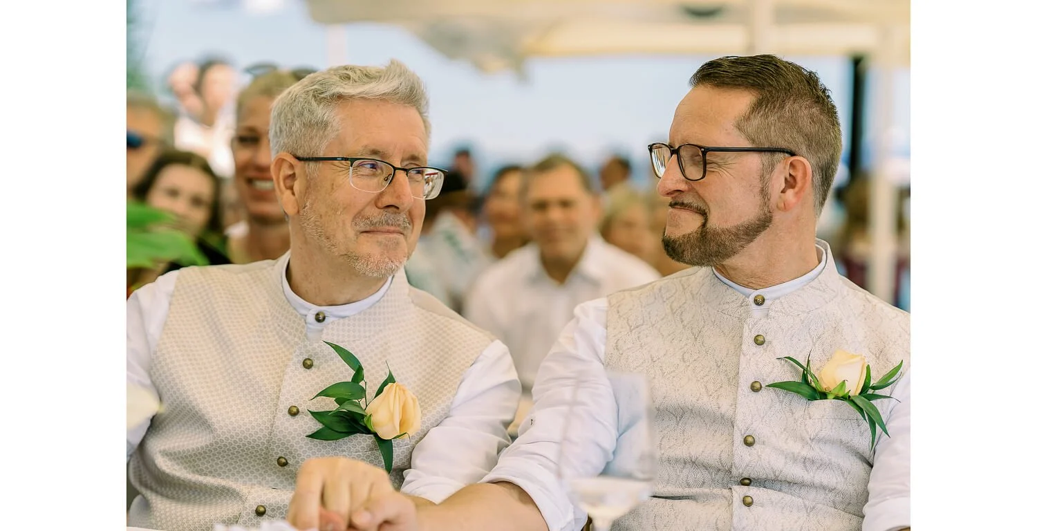 Zwei Männer sitzen nebeneinander bei ihrer standesamtlichen Hochzeit auf dem Floß in Lechbruck am See