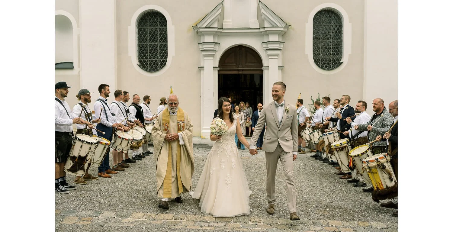 Brautpaar verlässt nach der kirchlichen Trauung das Kloster Irsee und geht durch ein Spalier aus Trommlern, begleitet vom Pfarrer