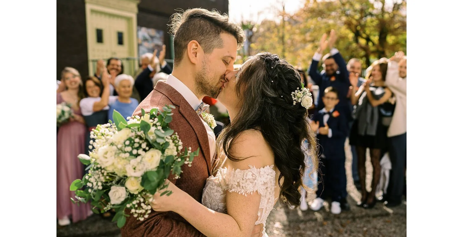 Brautpaar beim Kuss nach der Trauung vor dem Königlichen Jagdhaus in Oberstdorf, umgeben von engen Freunden