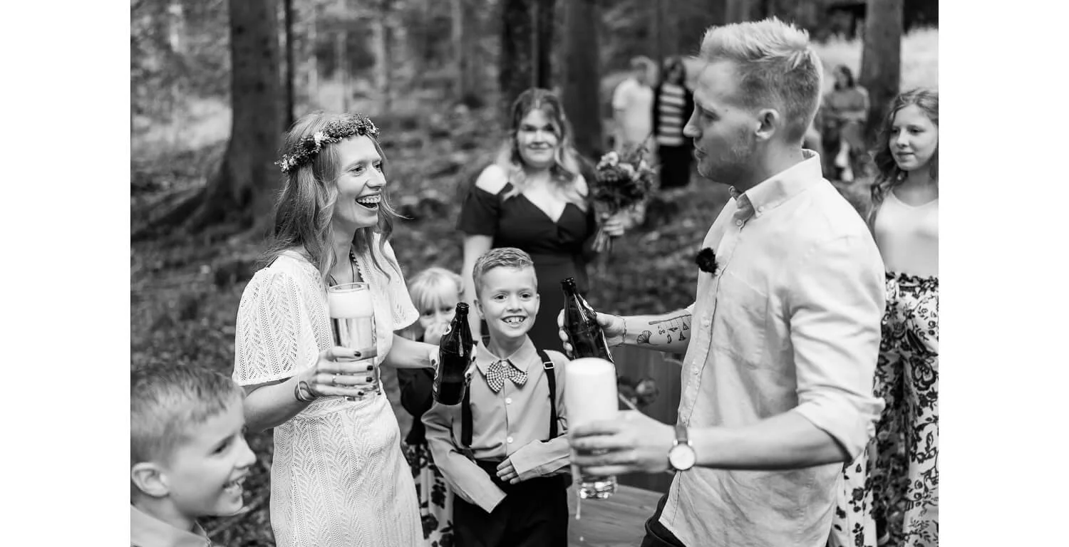 Brautpaar stößt mit Bier bei einer freien Trauung im Wald in Grainau an, umgeben von Gästen und Kindern