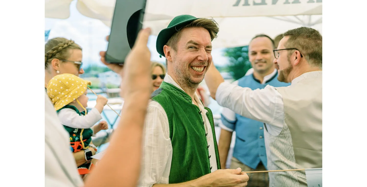 Gast in Tracht lacht während der Feier einer standesamtlichen Hochzeit auf einem Floß in Lechbruck am See