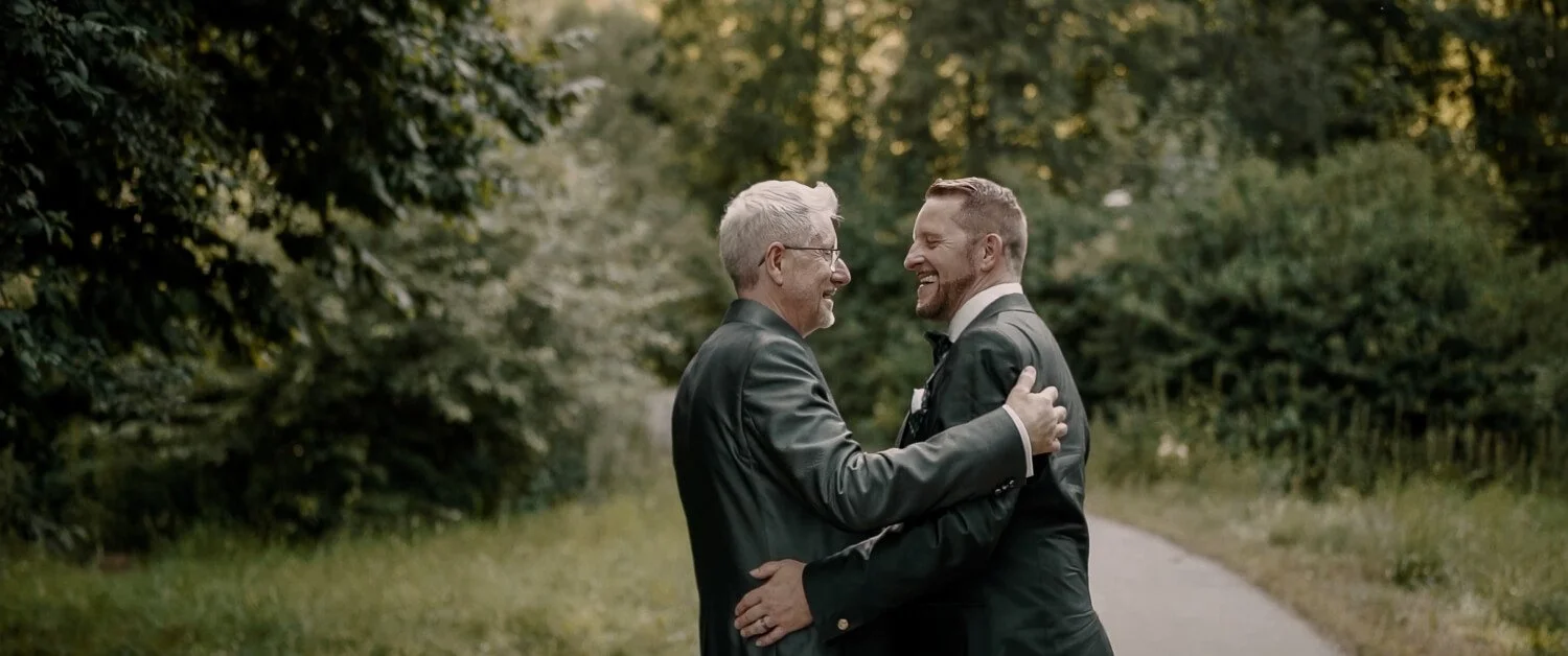 Zwei Männer lachen sich an und umarmen sich während ihres Paarshootings bei einer gleichgeschlechtlichen Hochzeit in Füssen.