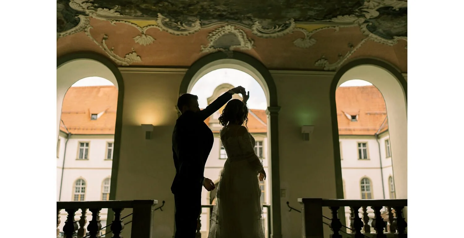 Tanzendes Brautpaar im Kreuzgang des Klosters St. Mang in Füssen, silhouettiert vor den Bögen nach der standesamtlichen Trauung