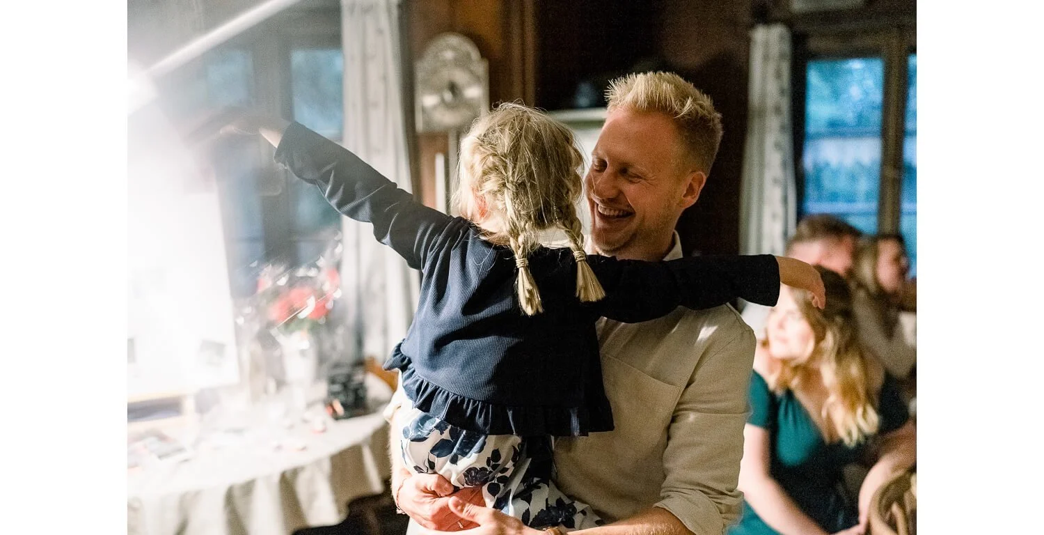 Bräutigam hält ein Kind lachend im Arm während der Hochzeitsfeier im Ferienhaus St. Hubertus in Grainau
