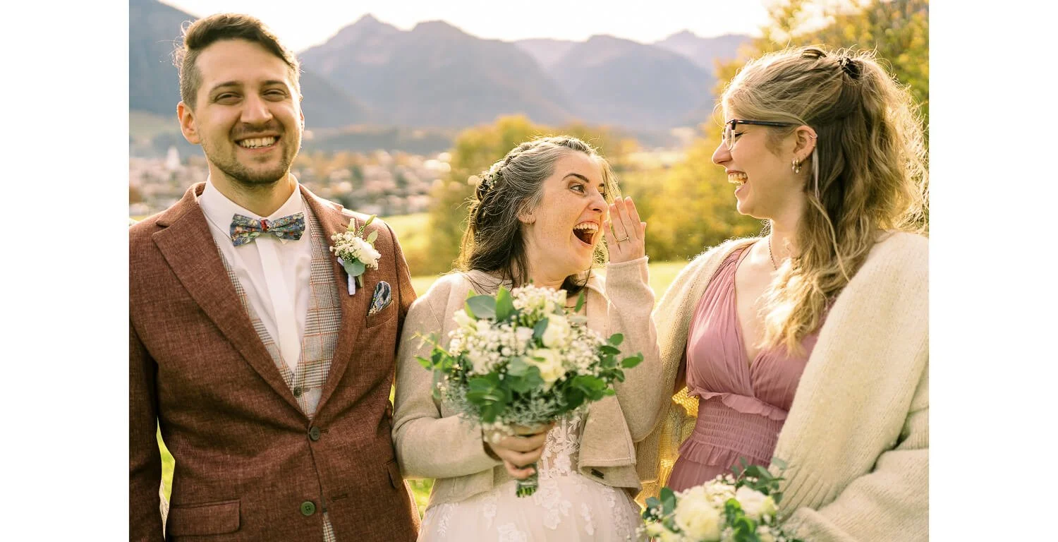 Braut und Bräutigam mit einer Freundin lachend vor der Bergkulisse in Oberstdorf