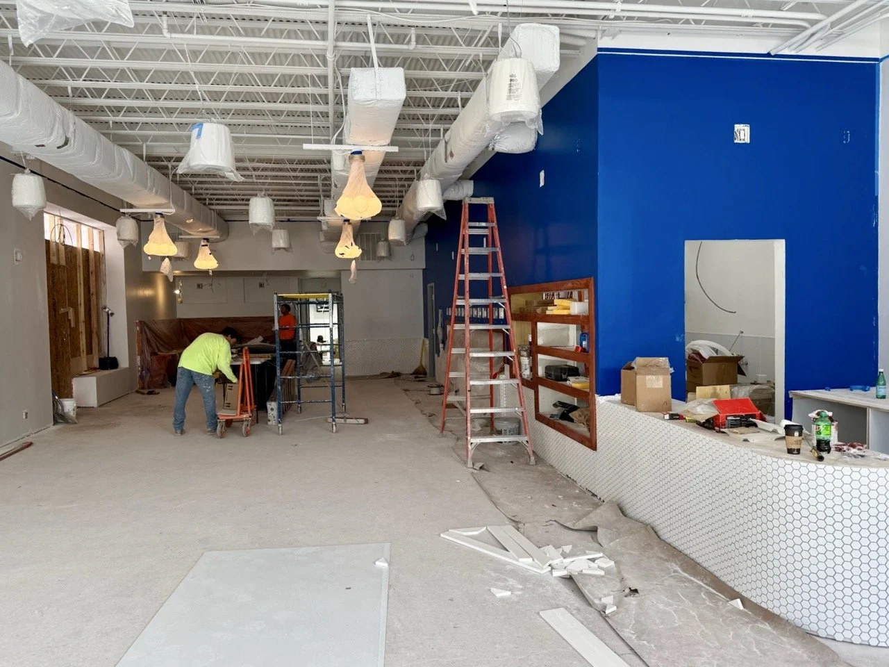 Interior under renovation with construction workers, ladders, construction materials, and partially finished walls.