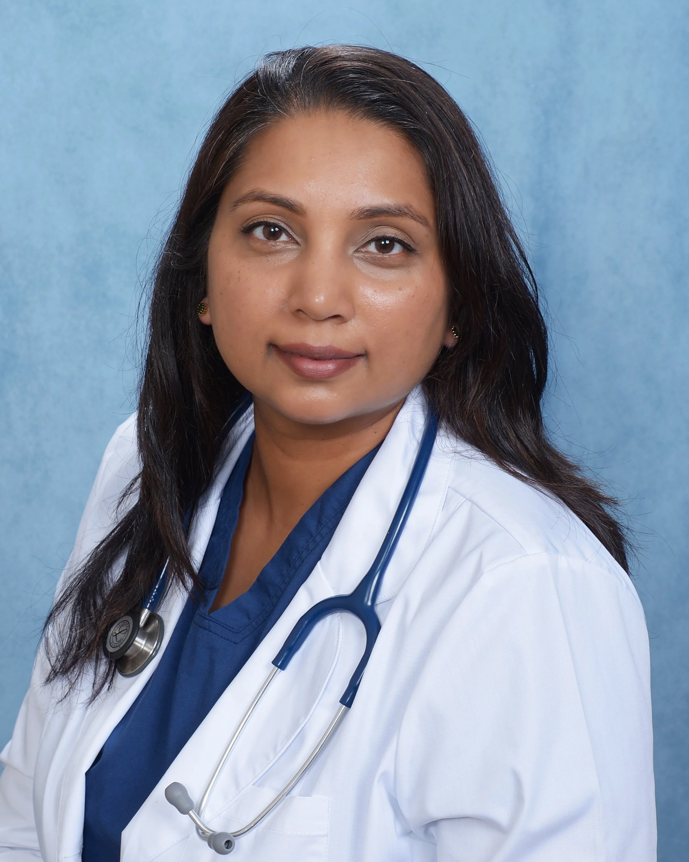 A medical professional, likely a doctor, wearing a white coat and a stethoscope, standing against a blue background.