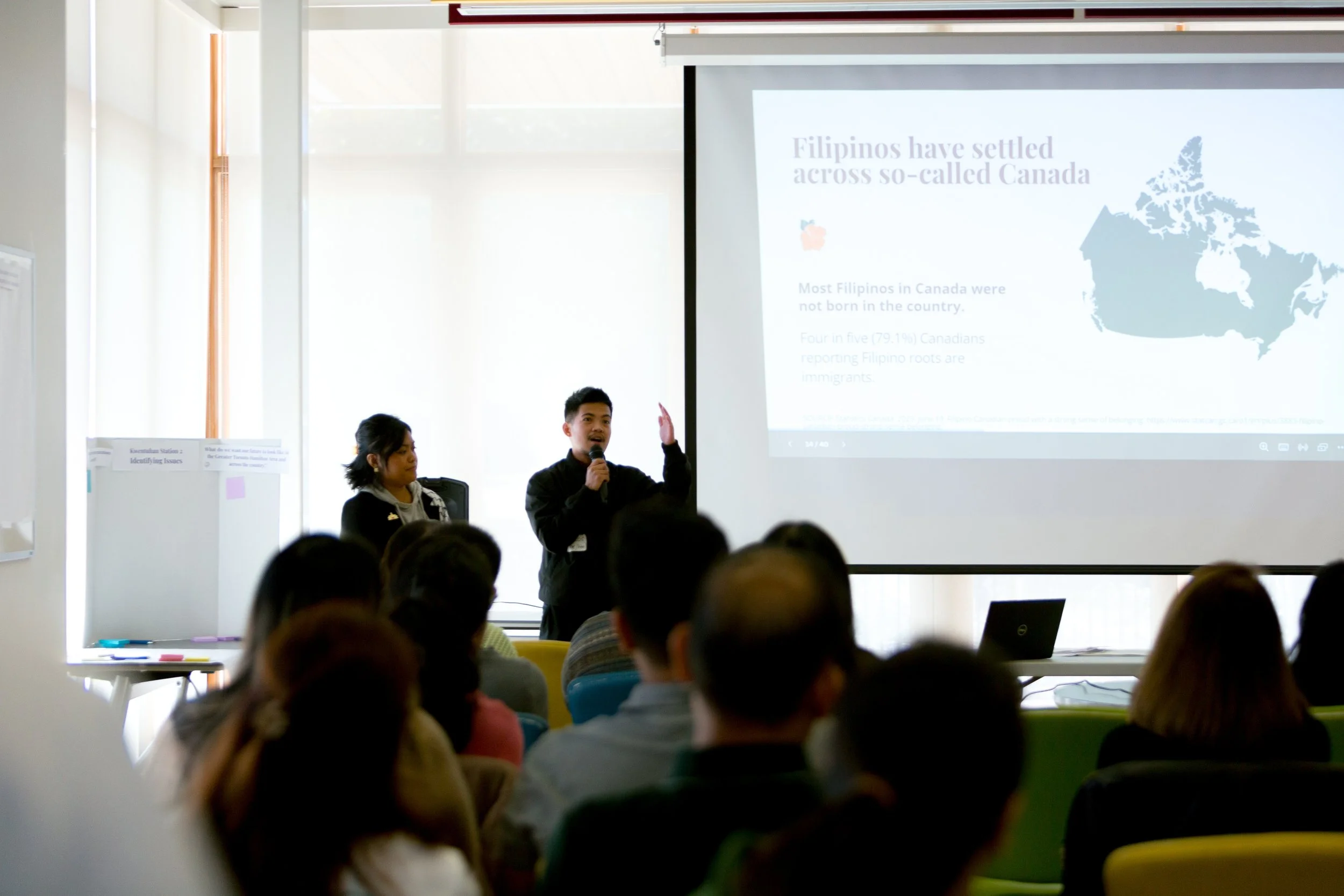 Two people talking to a room filled with people.