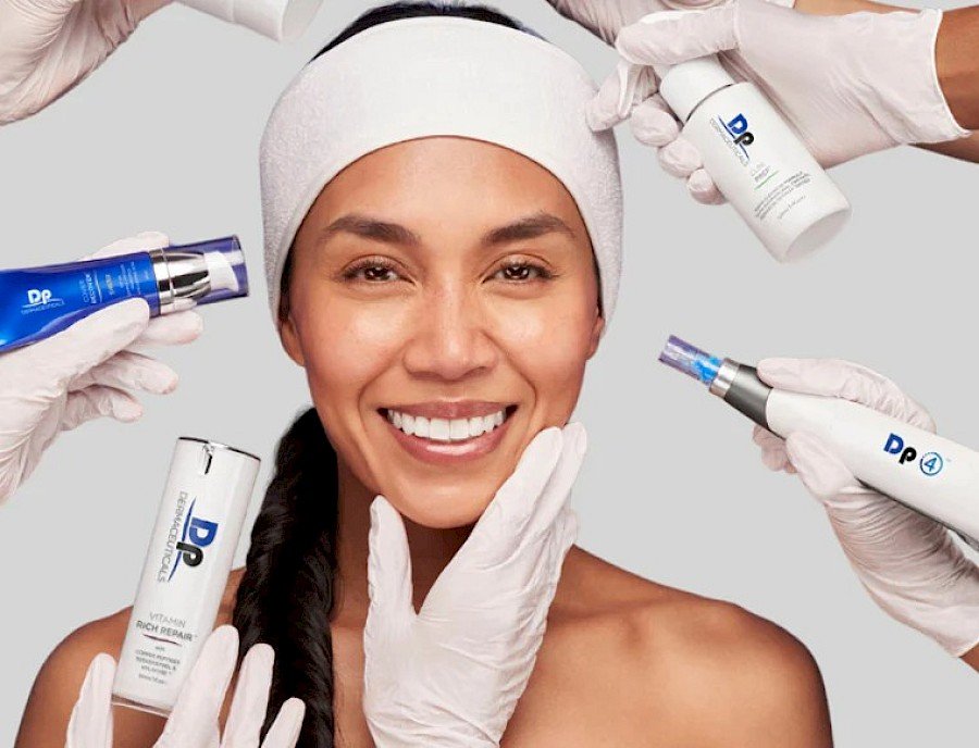 A woman smiling with skincare products being applied to her face by hands wearing white gloves.
