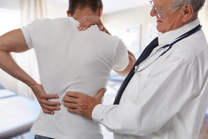 Doctor examining a patient's back and shoulder in a medical office.