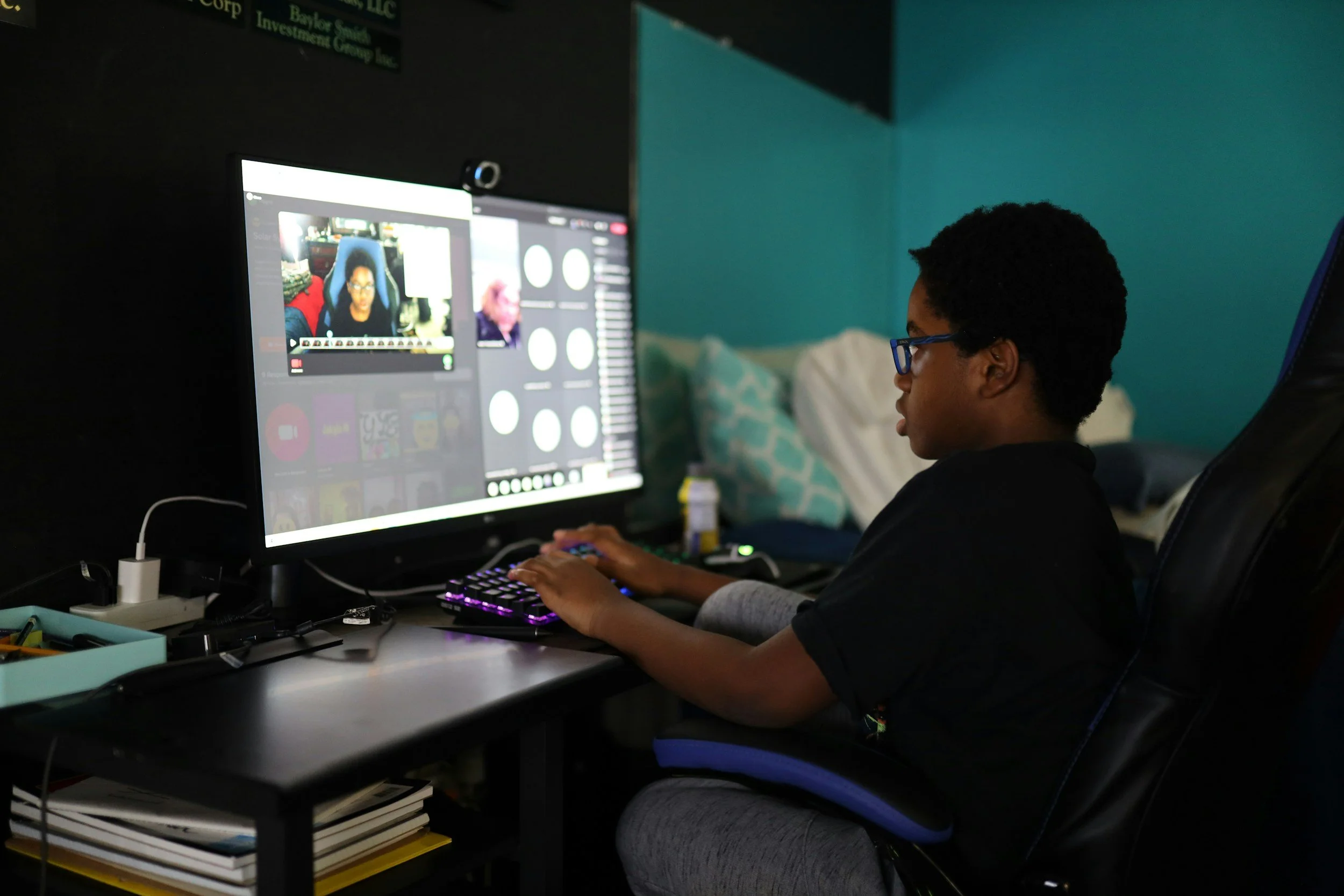A person with short curly hair and glasses sitting at a desk using a computer with a large monitor, engaged in video editing or gaming.